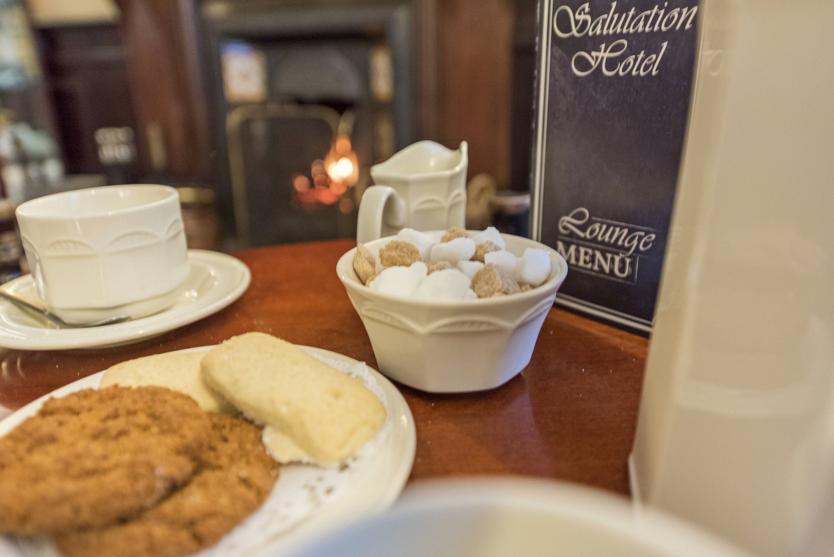 A table with a coffee cup, a bowl of marshmallows, and cookies. A menu is visible in the background.