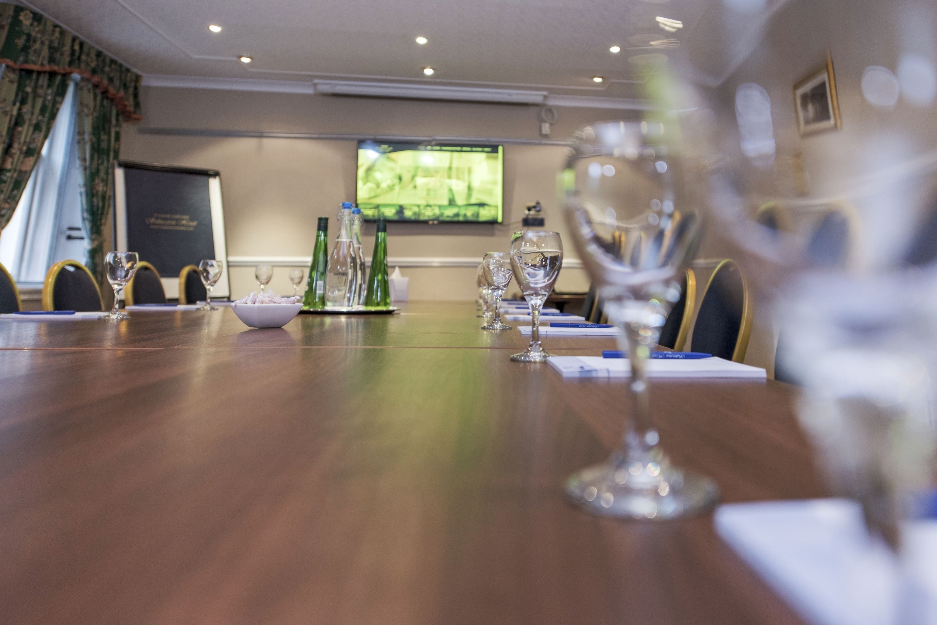A conference room with a long table, chairs, and a television screen in the background.