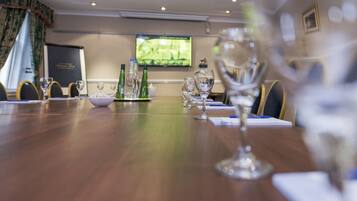 A conference room with a long table, chairs, and a television screen in the background.