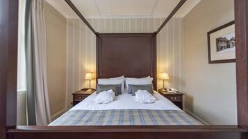 Habitación de hotel con una cama grande, dos mesitas de noche con lámparas, un cuadro enmarcado en la pared y una ventana con cortinas.
