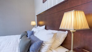 A neatly made bed with white and blue pillows, a wooden headboard, and a bedside lamp. - Salutation Hotel (Perth)