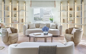 A modern living room with a beige sofa set, a round coffee table, and a bookshelf with decorative items.