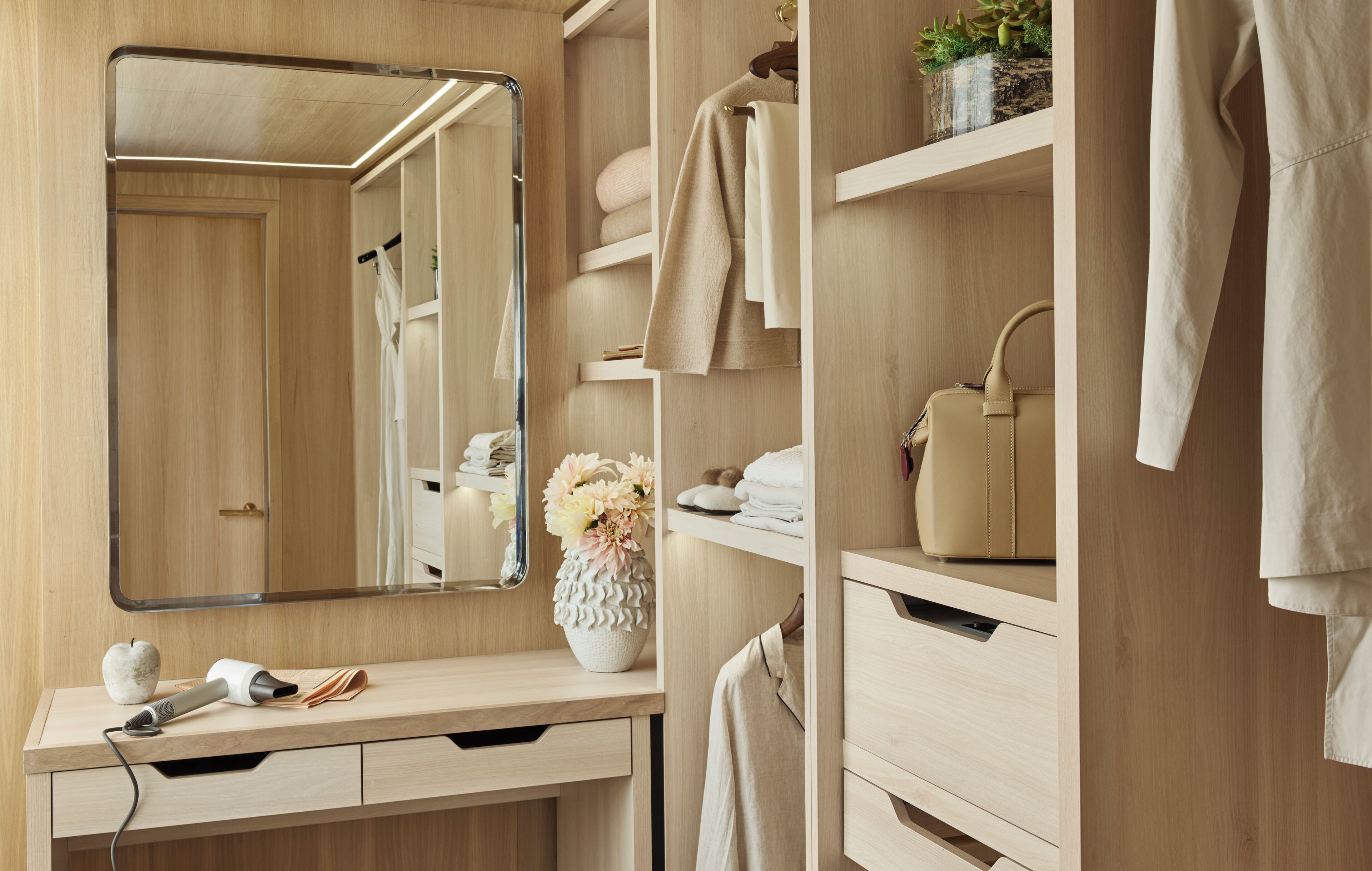 Een moderne badkamer met een houten wastafelmeubel, een spiegel en een plank met handdoeken en een bloevas.