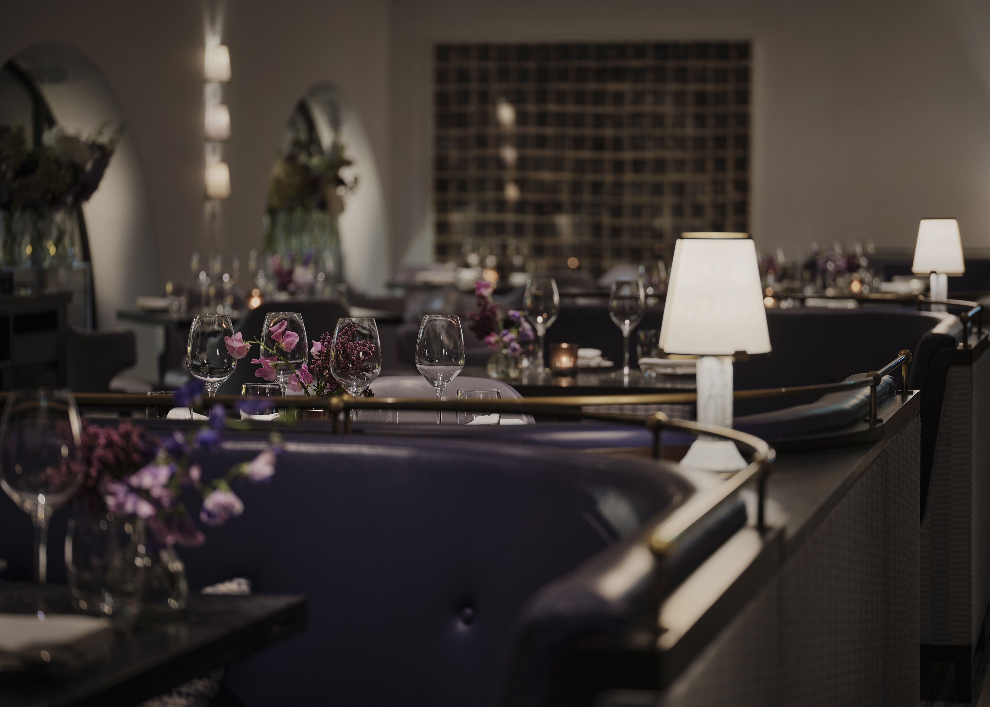 Un ambiente de restaurante con mesas dispuestas para comer, destacando copas de vino, flores y lámparas de mesa.