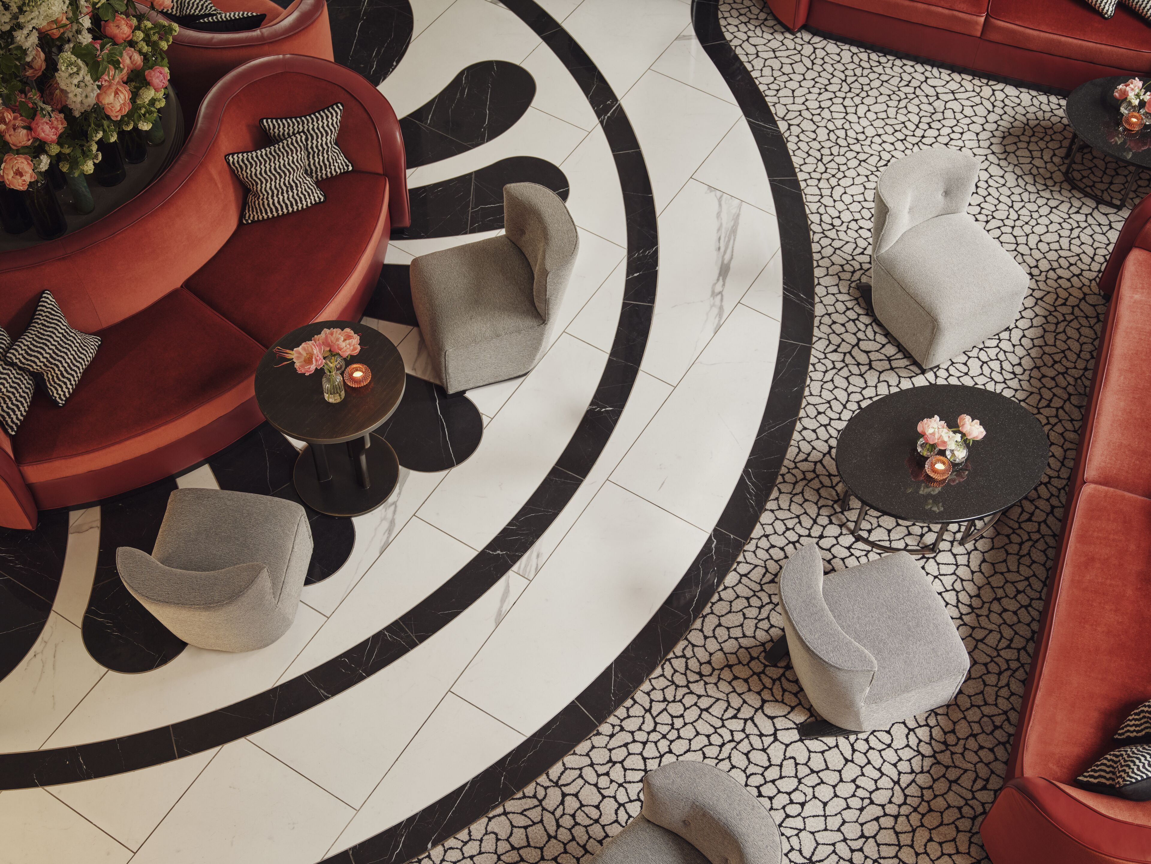 Ein moderner Lounge-Bereich mit einem roten Sofa, grauen Sesseln und einem schwarzen Couchtisch.