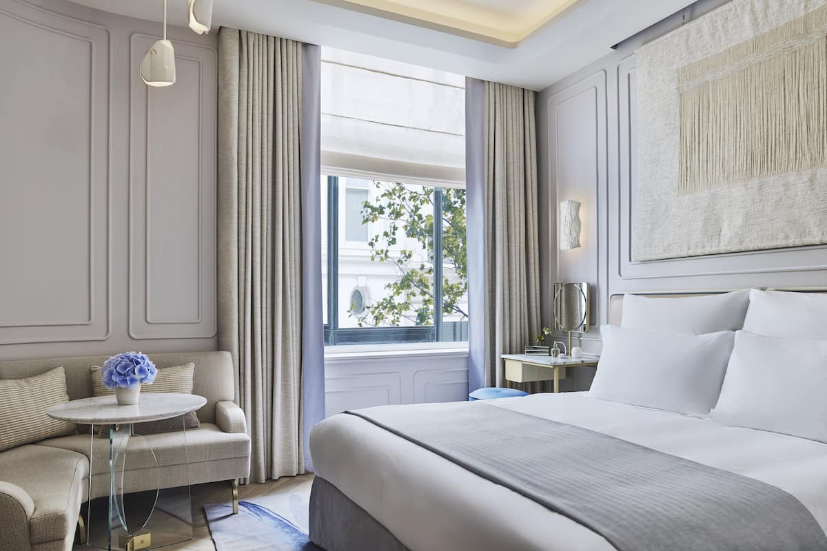 A modern hotel room with a large bed, a small round table, a sofa, and a desk with a lamp.