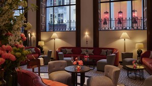 A hotel lobby with a red sofa, multiple armchairs, a coffee table, and a large window offering a view of a building with a 'THEATRE' sign. - One Aldwych (London)