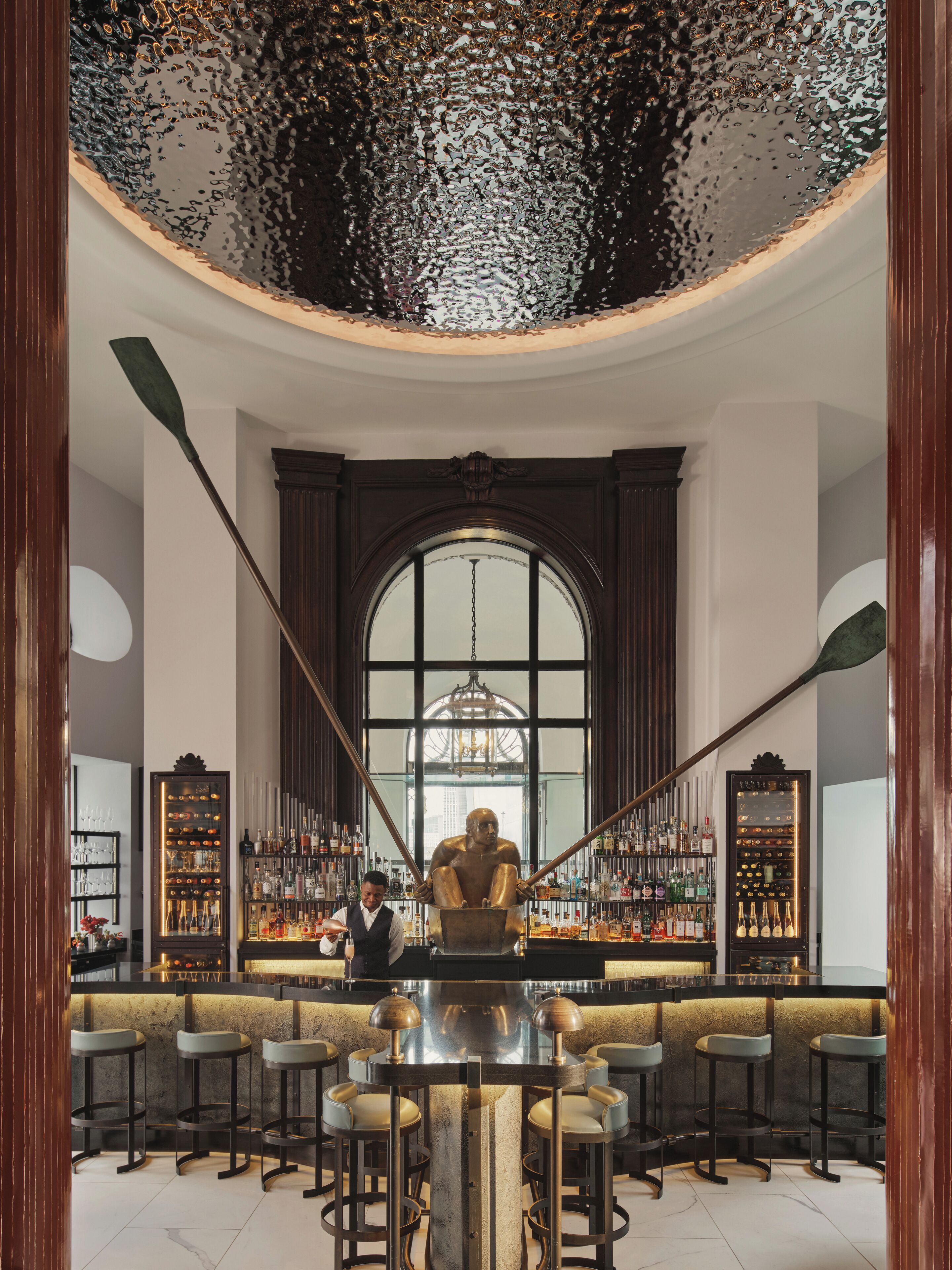 A bar area with a central bar counter, stools, and a bartender.