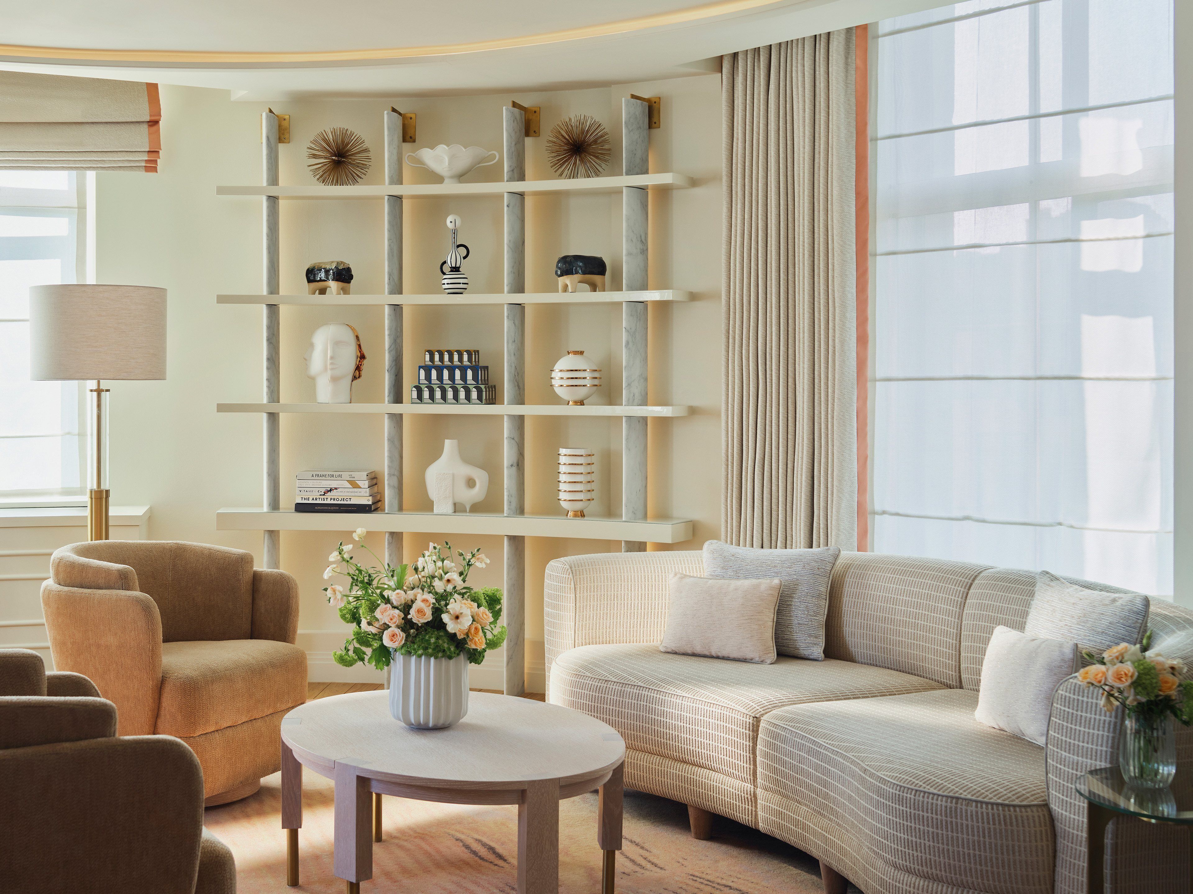 Een moderne woonkamer met een bank, fauteuils, een salontafel en een boekenkast met decoratieve objecten.