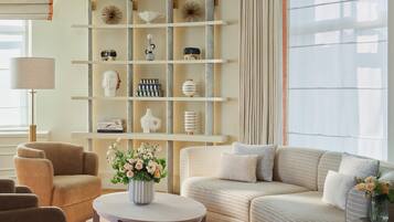 Een moderne woonkamer met een bank, fauteuils, een salontafel en een boekenkast met decoratieve objecten.