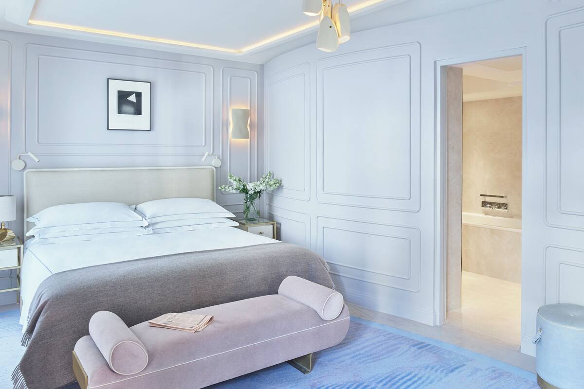 A modern bedroom with a large bed, bedside tables, a nightstand, and a bathroom visible through an open door.