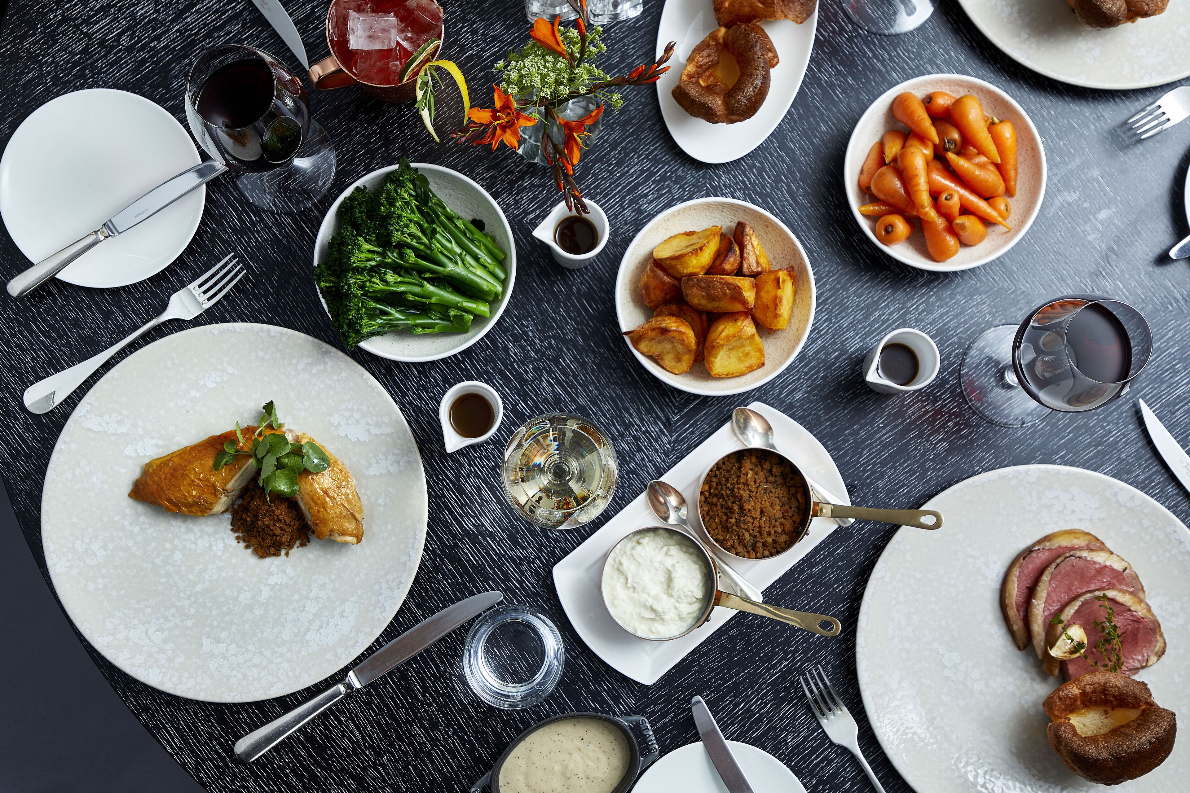 Una mesa dispuesta con diversos platos, incluyendo patatas asadas, zanahorias y un guiso de carne, junto con varias copas de vino.