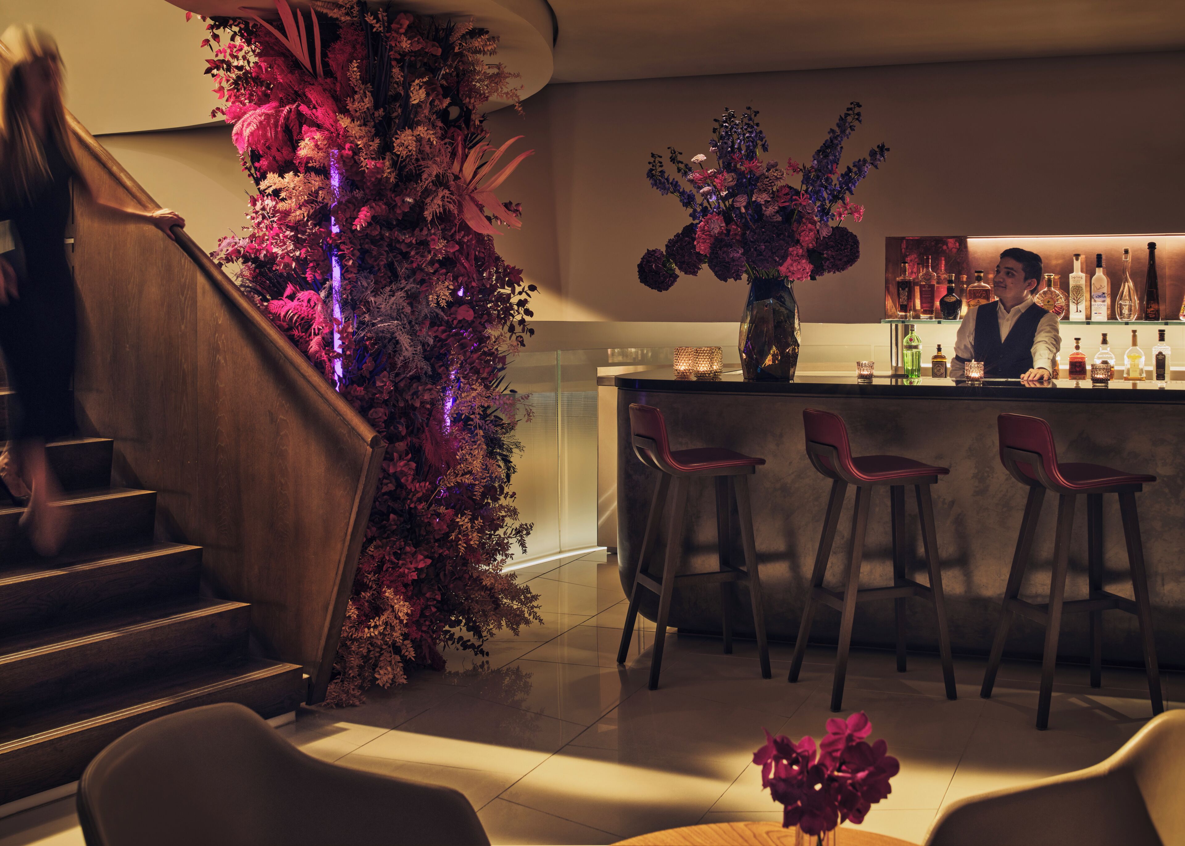 Uma área de bar com escadas, banquetas e balcão com garrafas.