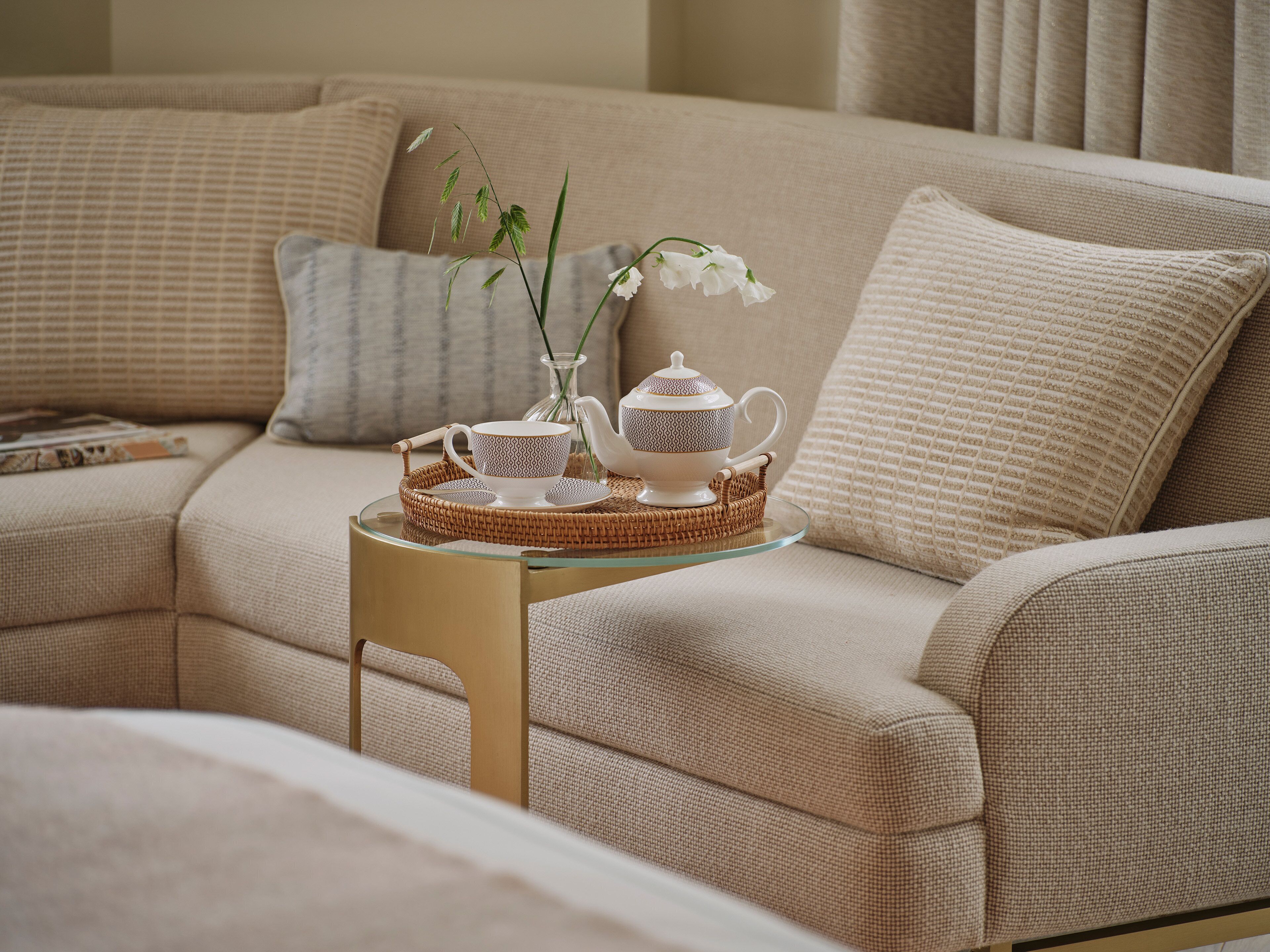Ein gemütliches Wohnzimmer mit einem beigen Sofa, einem Glastisch und einem dekorativen Teeservice.