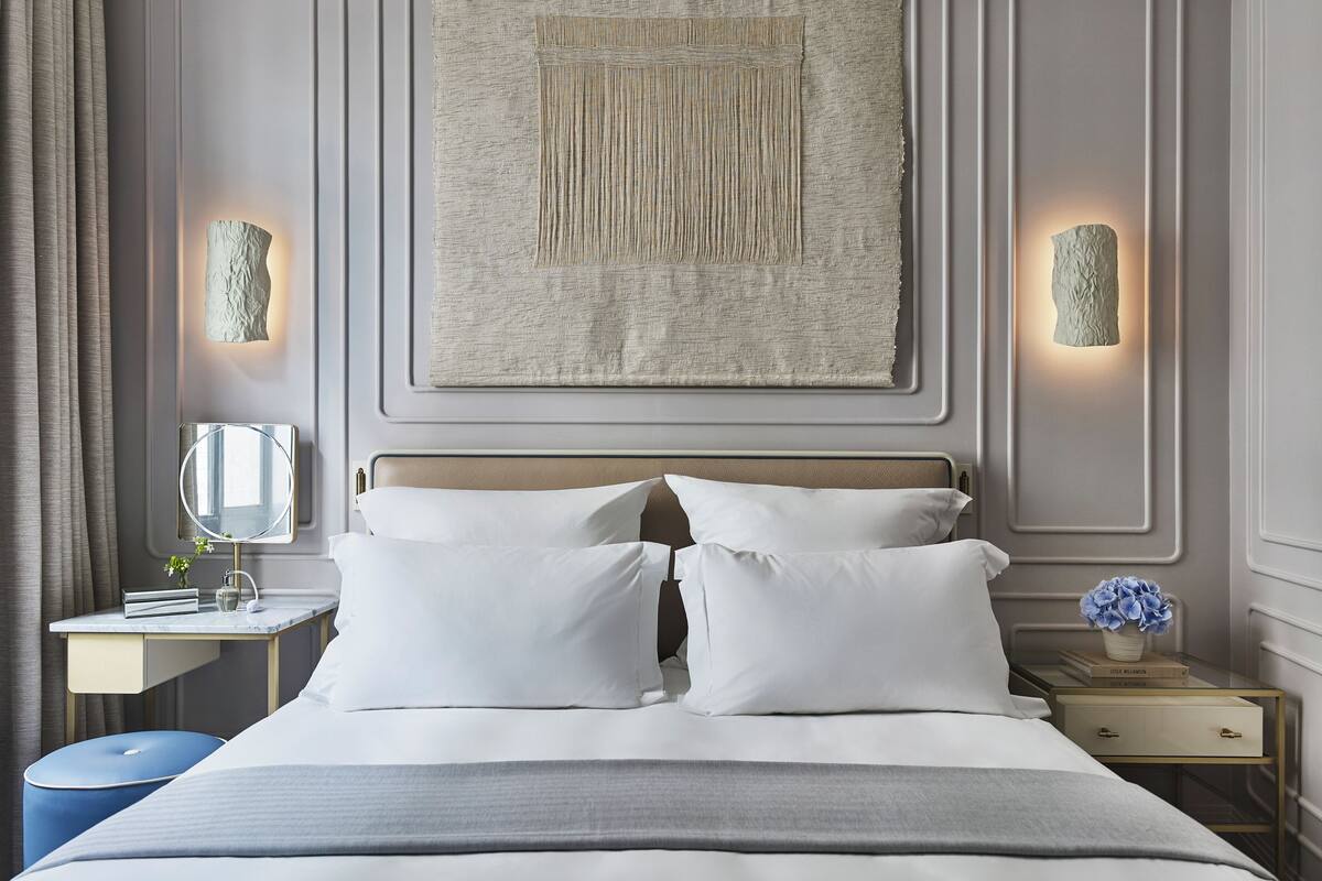 A neatly arranged hotel room with a bed, bedside tables, a mirror, and a wall-mounted artwork.