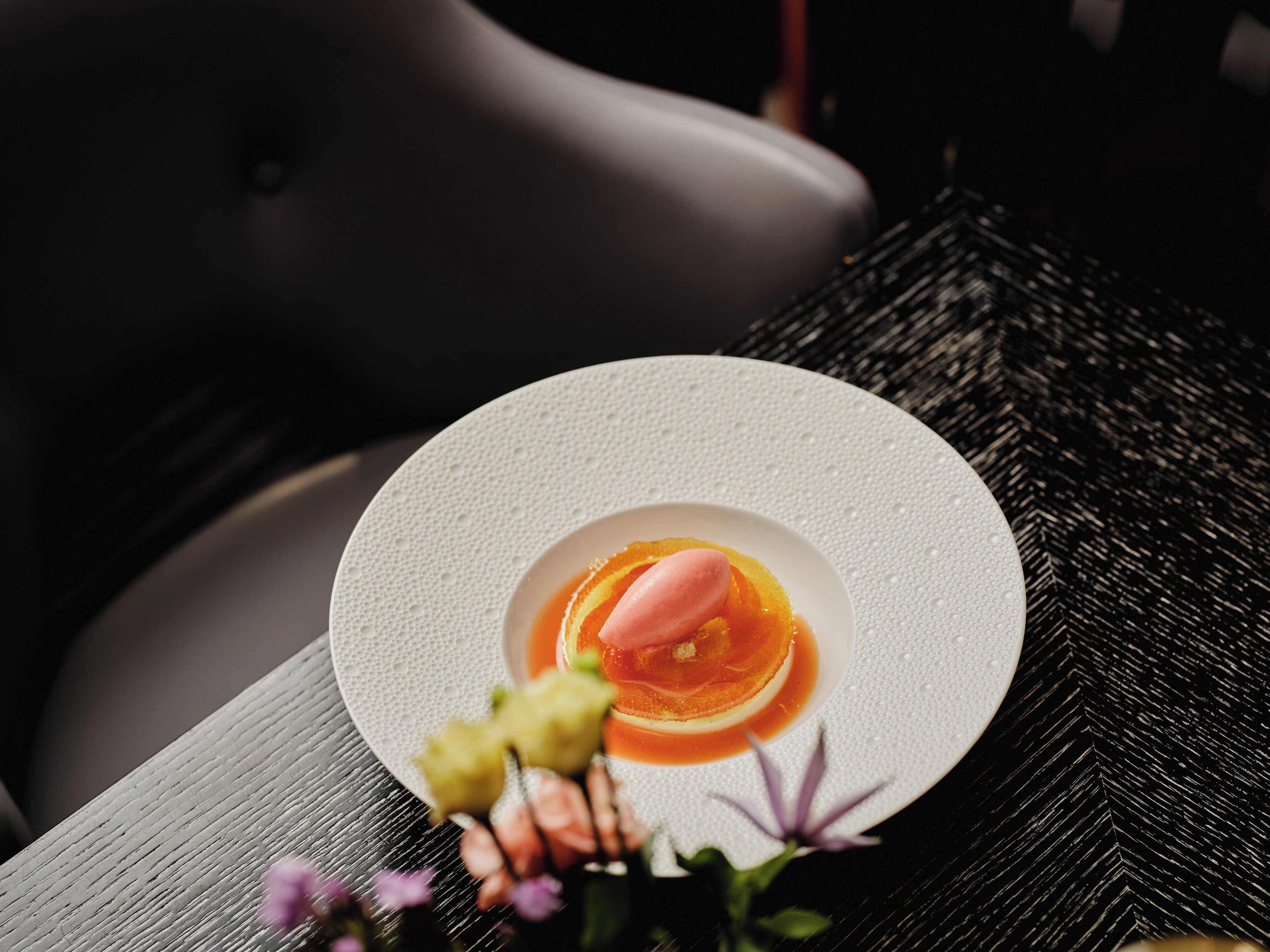Une assiette blanche sur laquelle est présentée une pâtisserie, le tout posé sur une surface texturée.