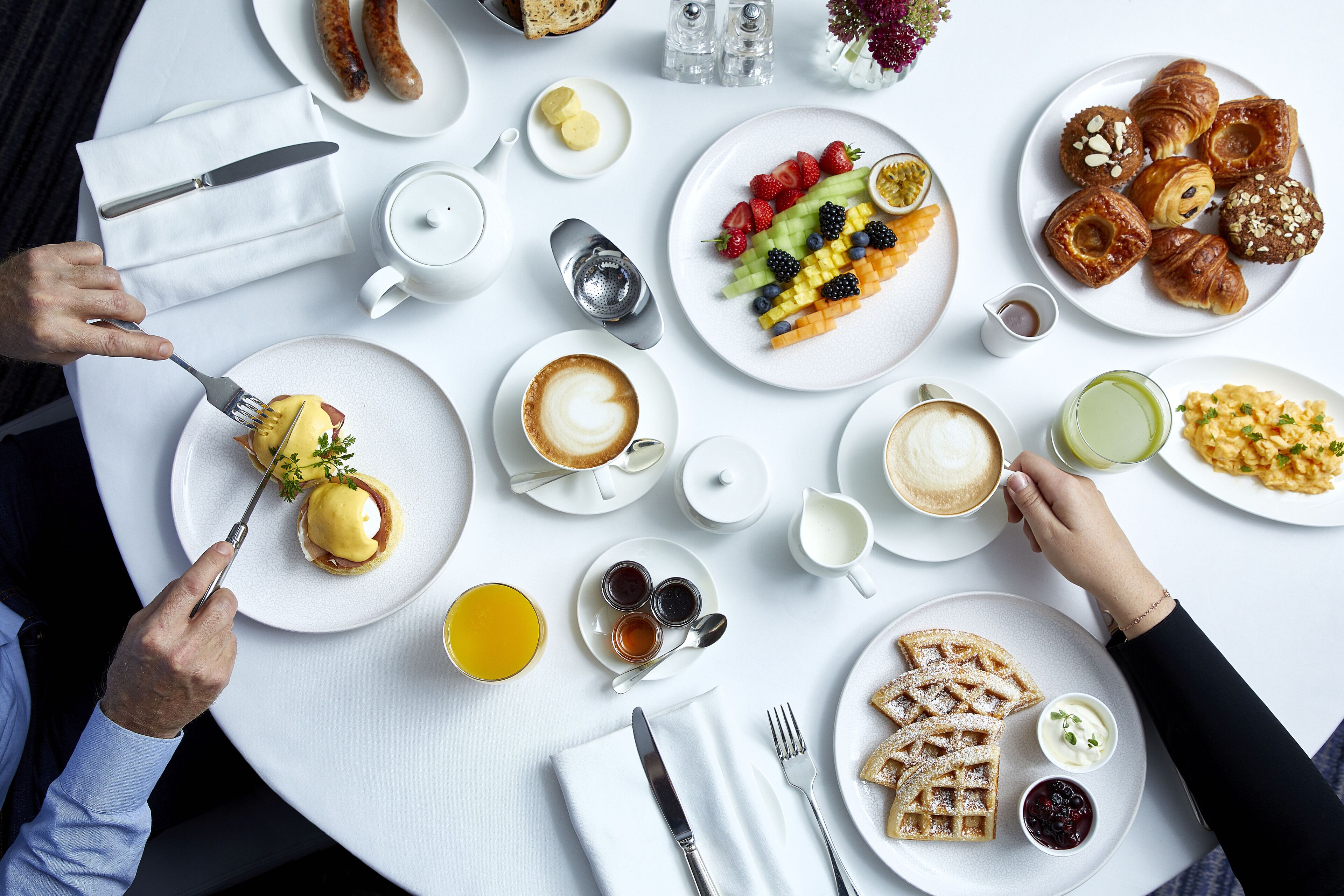 A breakfast setting with various dishes, utensils, and beverages on a round table.