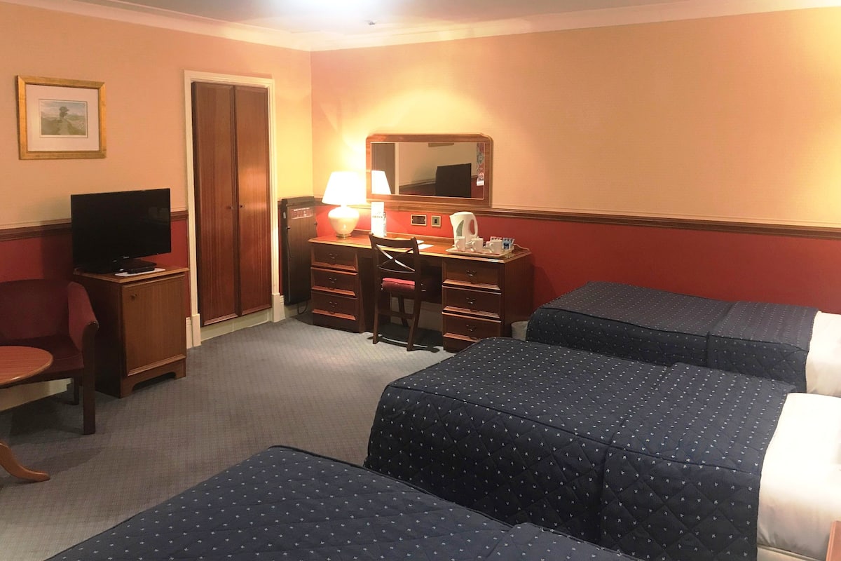 A hotel room with two beds, a desk with a lamp, a television, and a chair.
