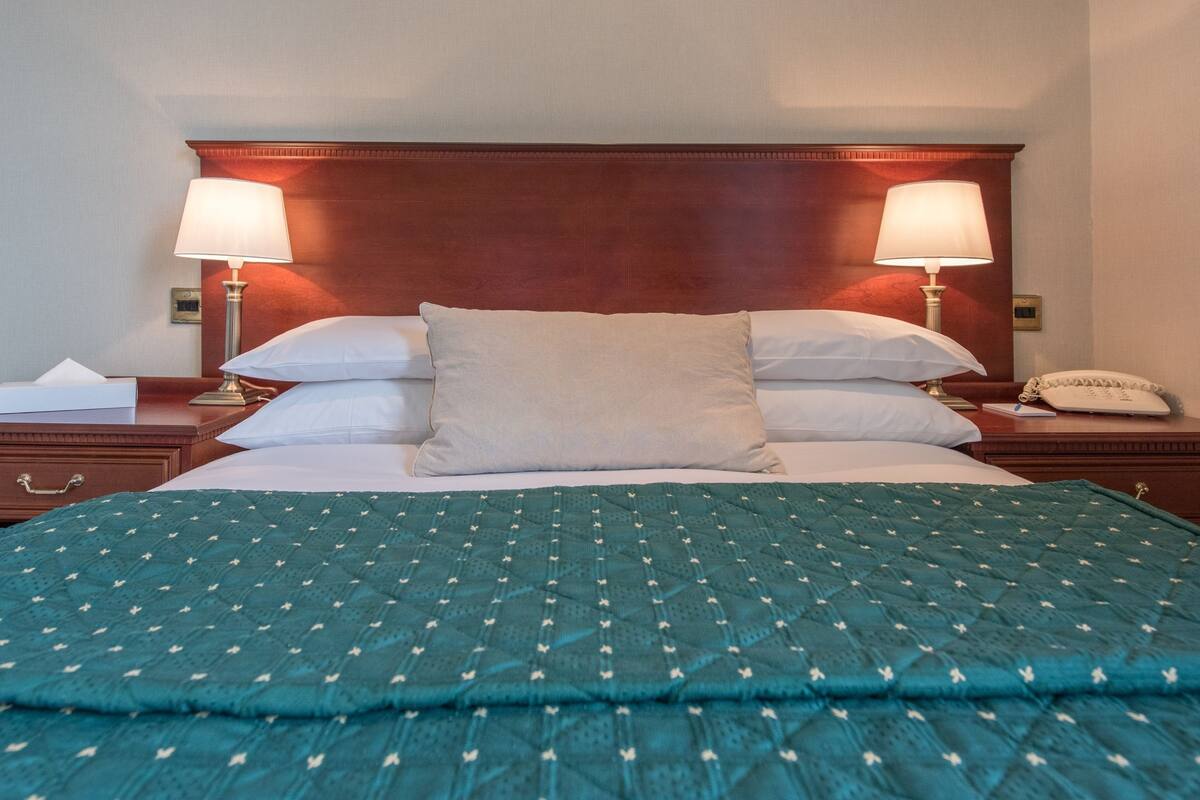 A hotel room with a large bed, two bedside lamps, a nightstand with a phone, and a wooden headboard.