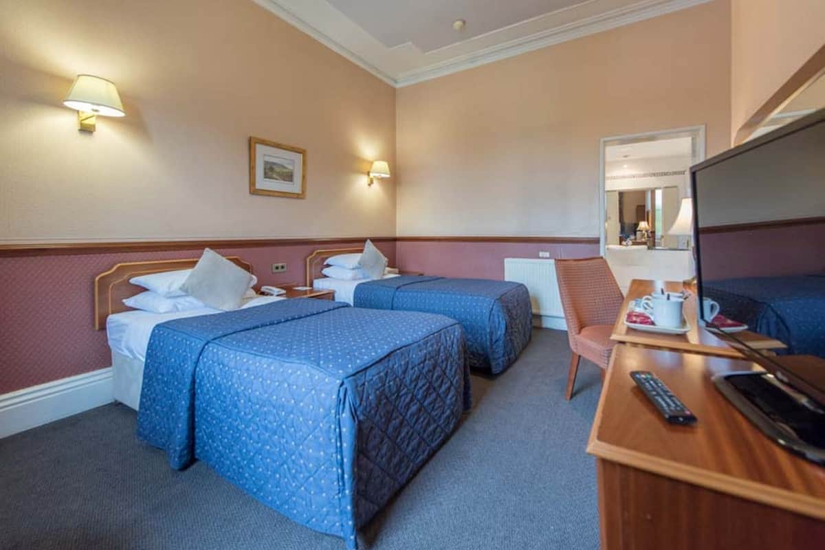 A hotel room with two beds, a desk with a laptop, a chair, and a TV.
