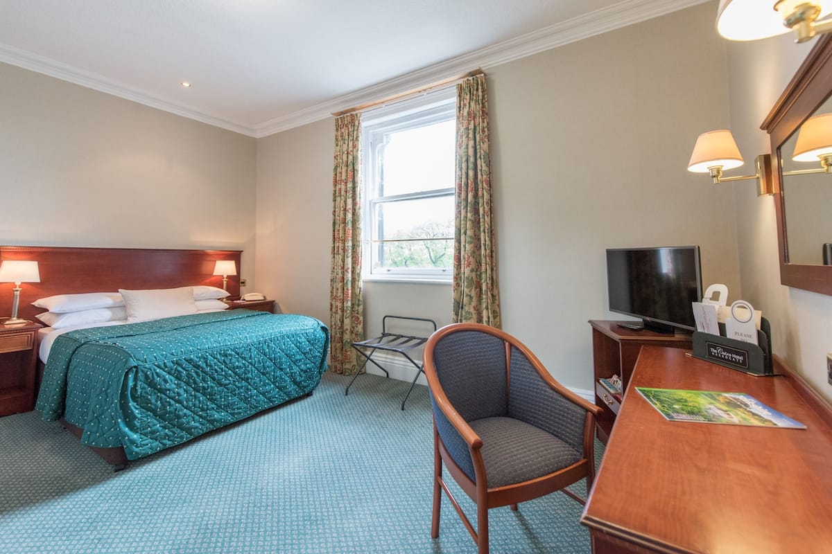 A hotel room with a bed, a desk, a chair, a television, and a window with curtains.