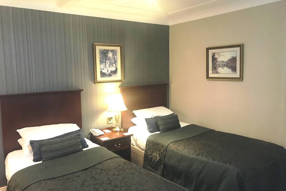 A hotel room with two beds, a nightstand, a lamp, and two framed pictures on the wall.