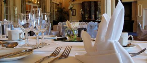 Una mesa formal dispuesta con servilletas blancas, cubiertos y copas de vino.
