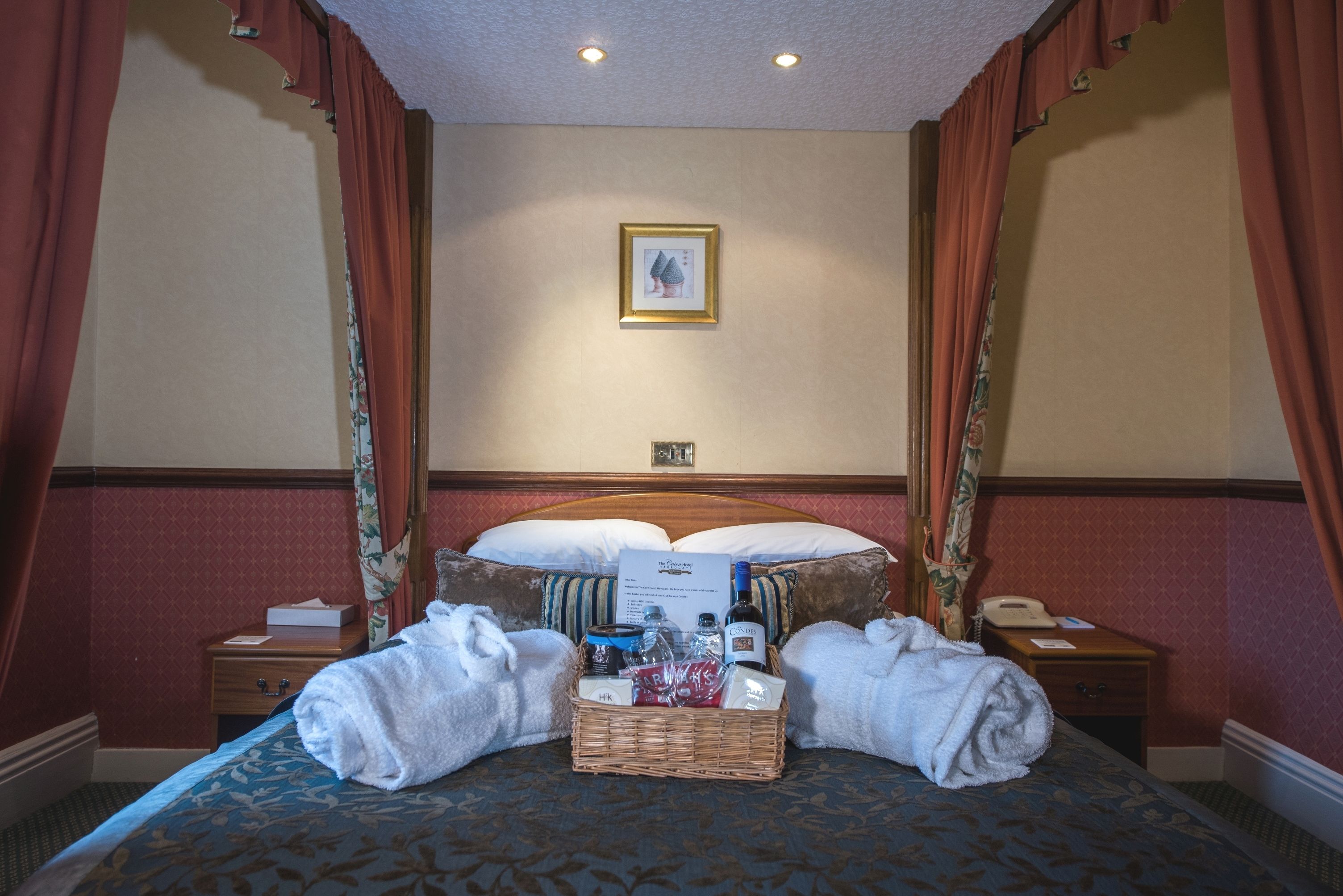 A hotel room with a large bed, a bedside table with a lamp, a framed picture on the wall, and a window with curtains.