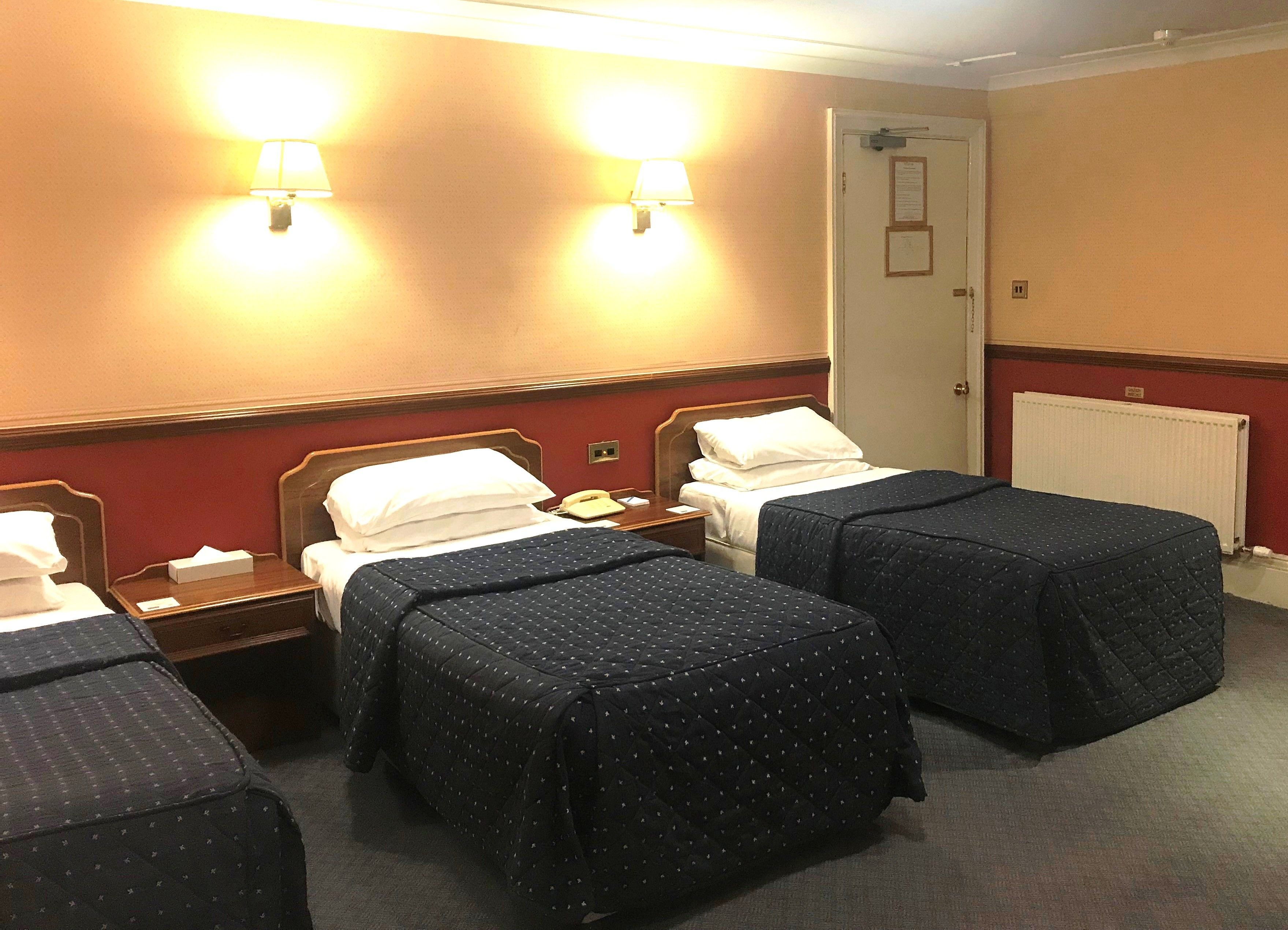 Een hotelkamer met twee eenpersoonsbedden, een nachtkastje met een lamp en een deur met een berichtje.
