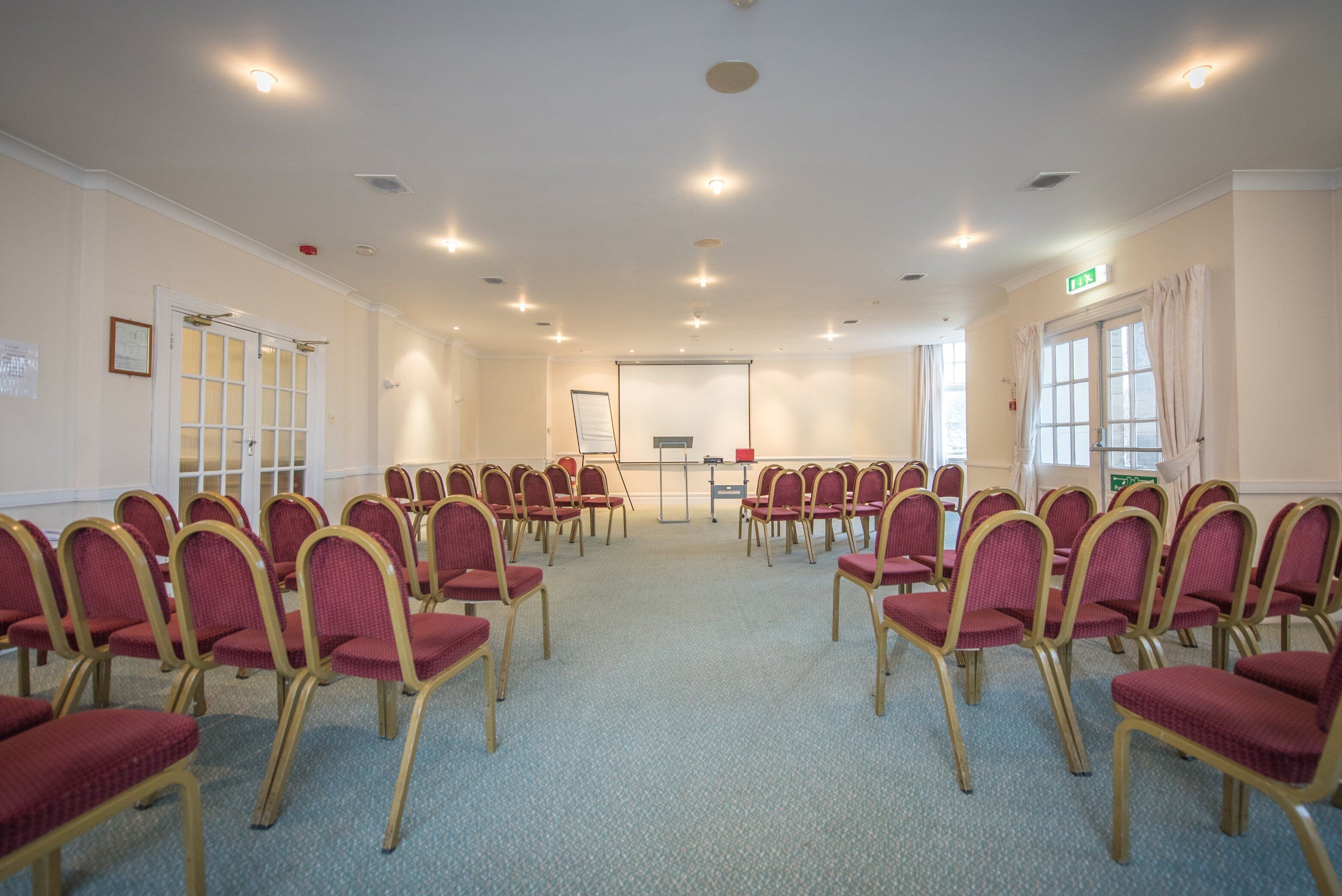 A conference room with rows of chairs facing a presentation screen, a whiteboard, and a projector.