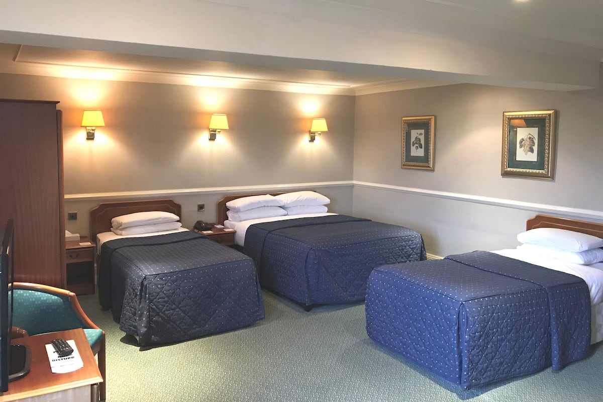 A hotel room with two beds, a desk with a chair, and a small table with a remote control.