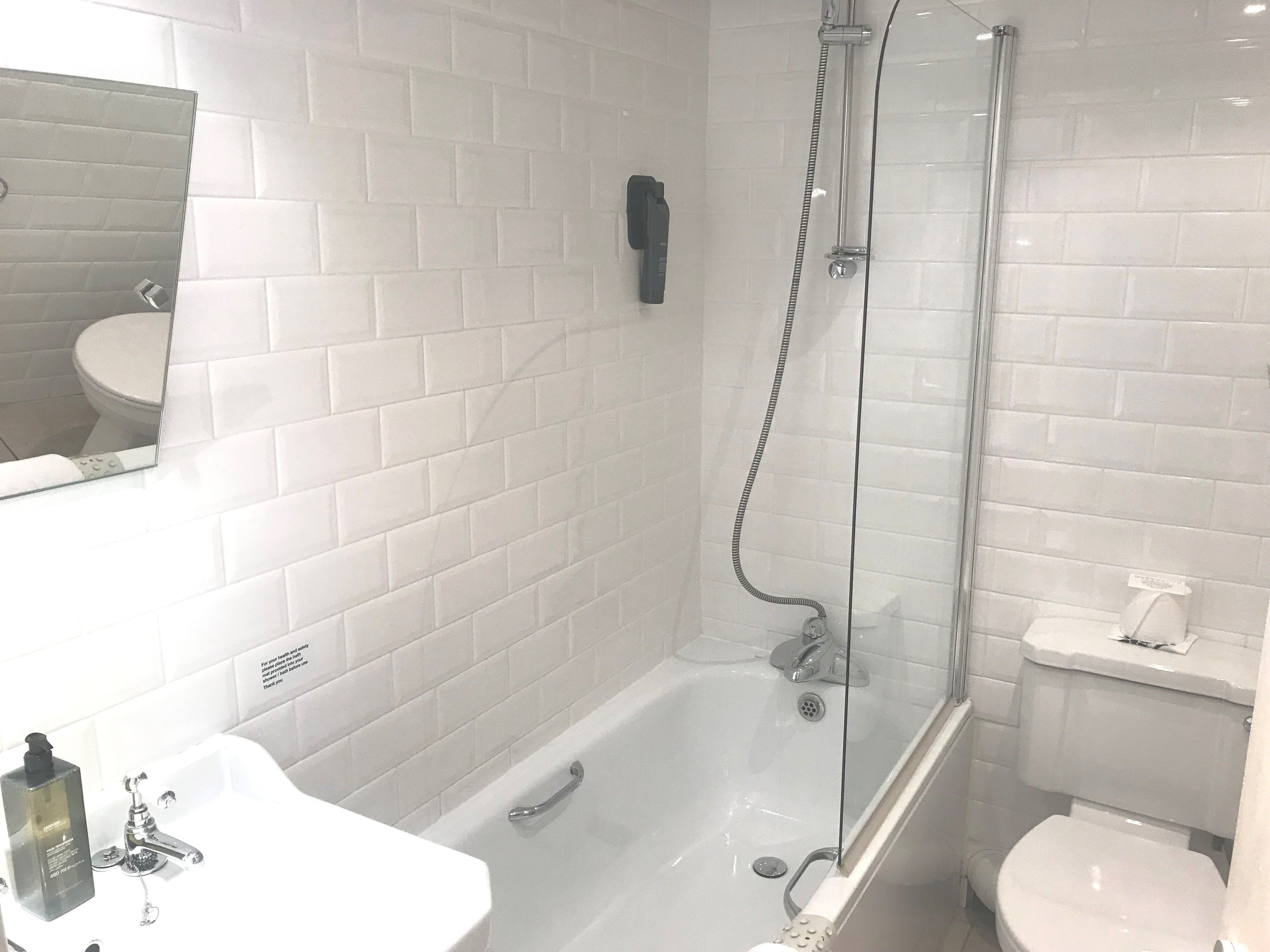 A modern bathroom with a glass-enclosed shower, a white bathtub, and a sink with a soap dispenser.