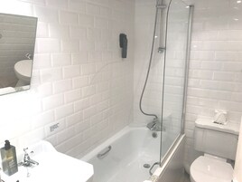 A modern bathroom with a glass-enclosed shower, a white bathtub, and a sink with a soap dispenser.