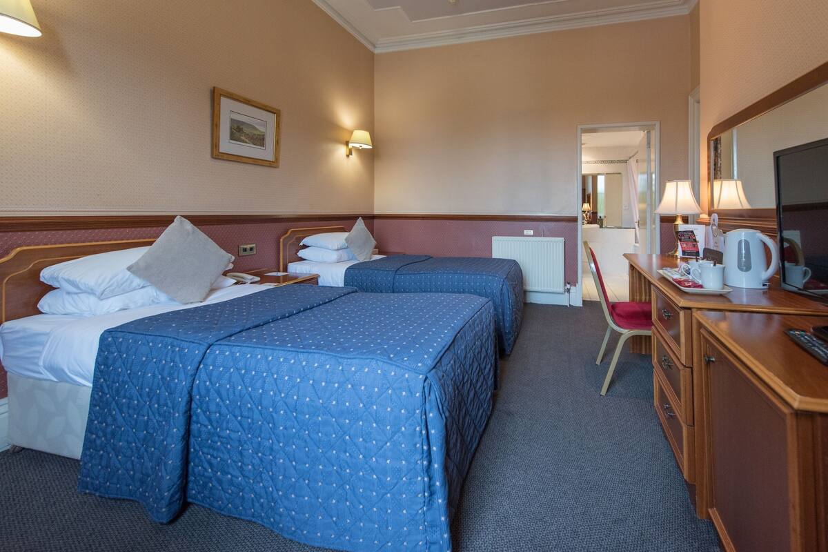 A hotel room with two beds, a desk with a chair, a television, and a mirror.