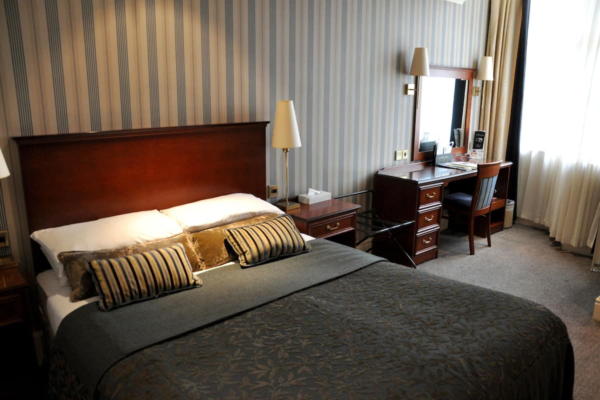 A hotel room with a large bed, a desk, a chair, a lamp, and a mirror.
