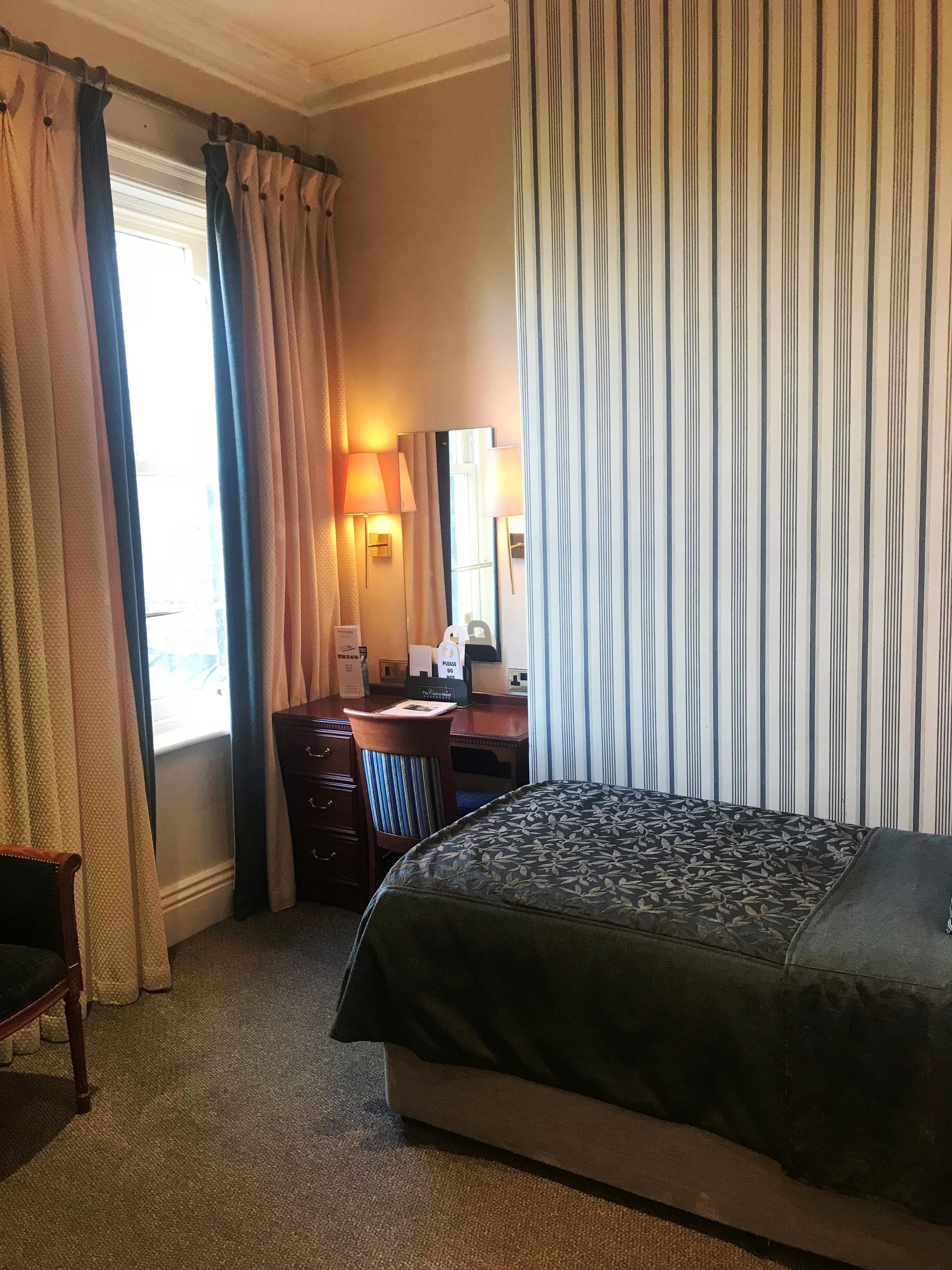 A hotel room with a bed, a desk, a chair, and a window with curtains.