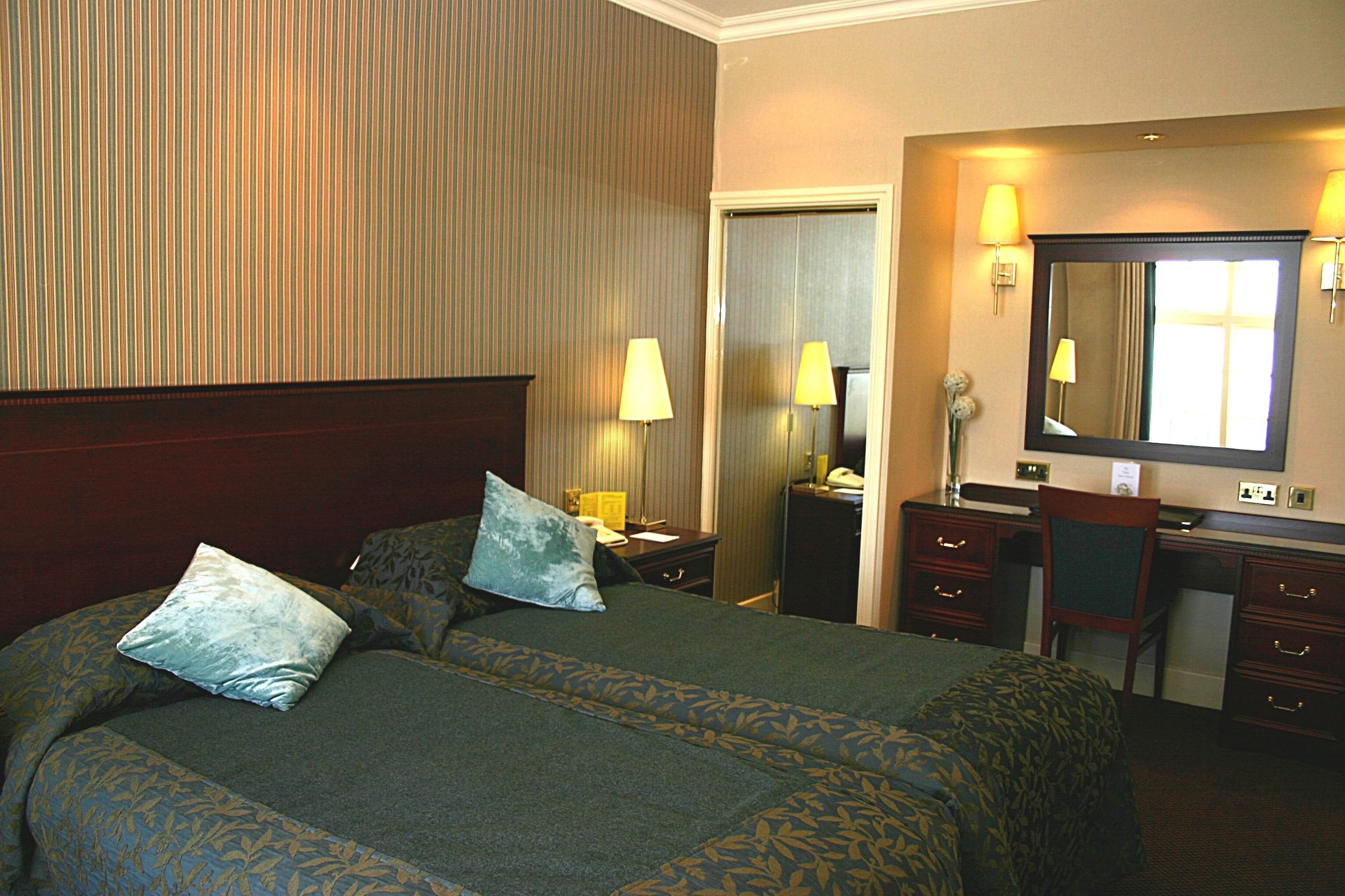 A hotel room with a large bed, two bedside tables, a desk, a chair, a mirror, and a door.