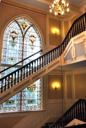 A grand staircase with a chandelier, ornate stained glass windows, and a polished wooden finish. - Cairn Hotel (Harrogate)