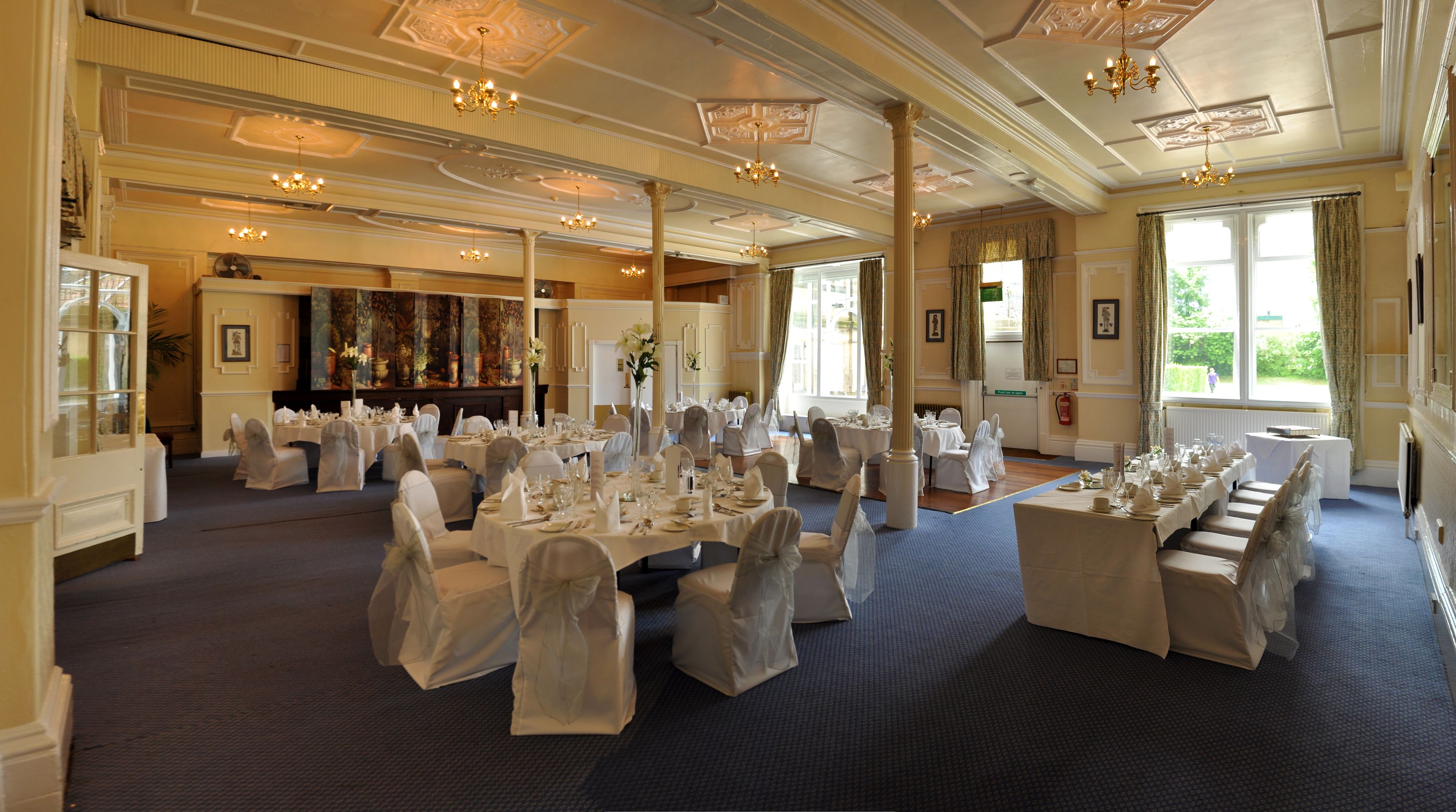 A banquet hall with multiple round tables set for events, large windows, and classical architectural details.
