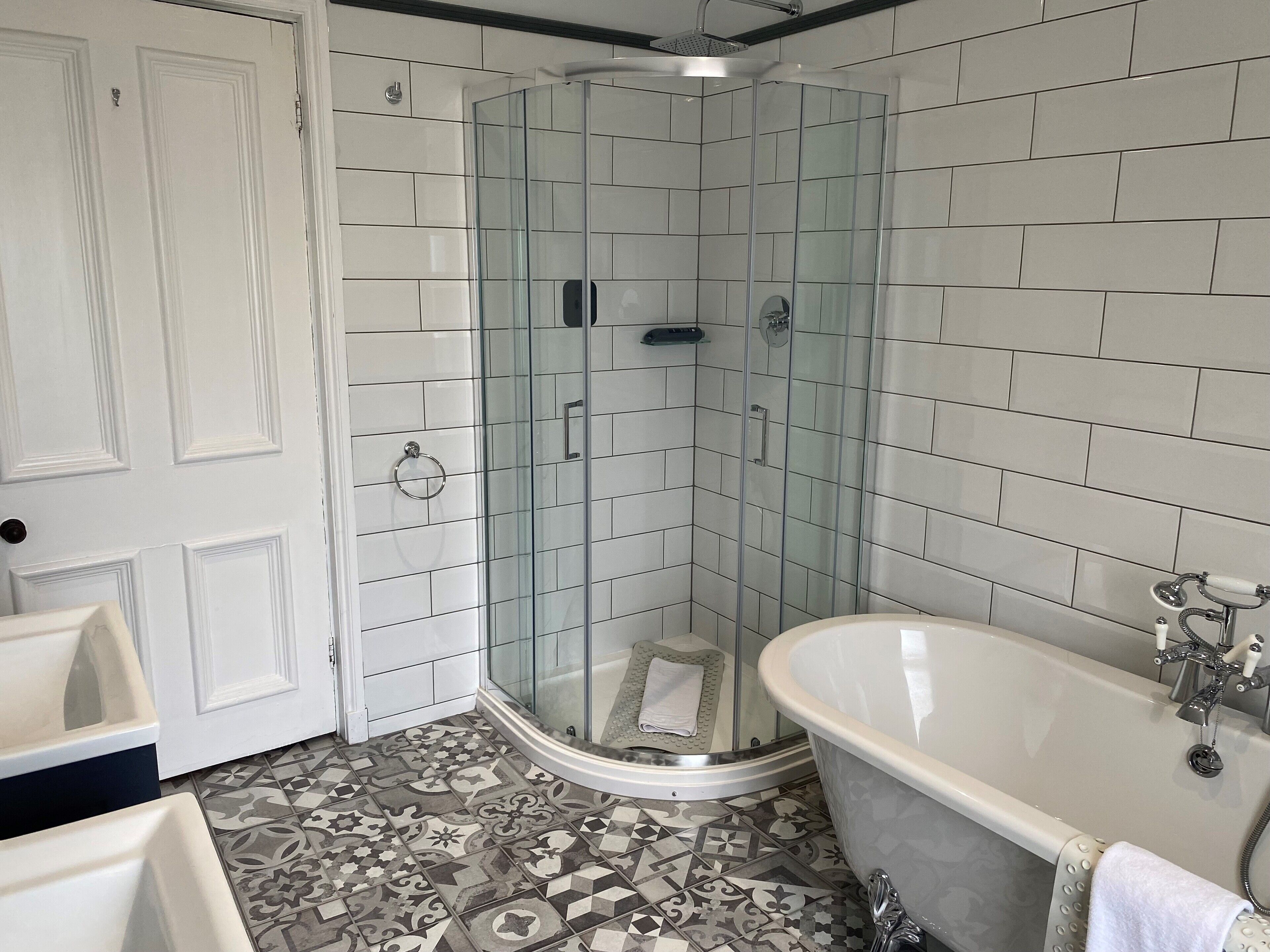 A bathroom with a glass-enclosed shower, a freestanding bathtub, and patterned floor tiles.