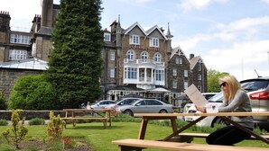 A woman sitting at a picnic table in front of a historic building with a stone facade and multiple windows. - Cairn Hotel (Harrogate)