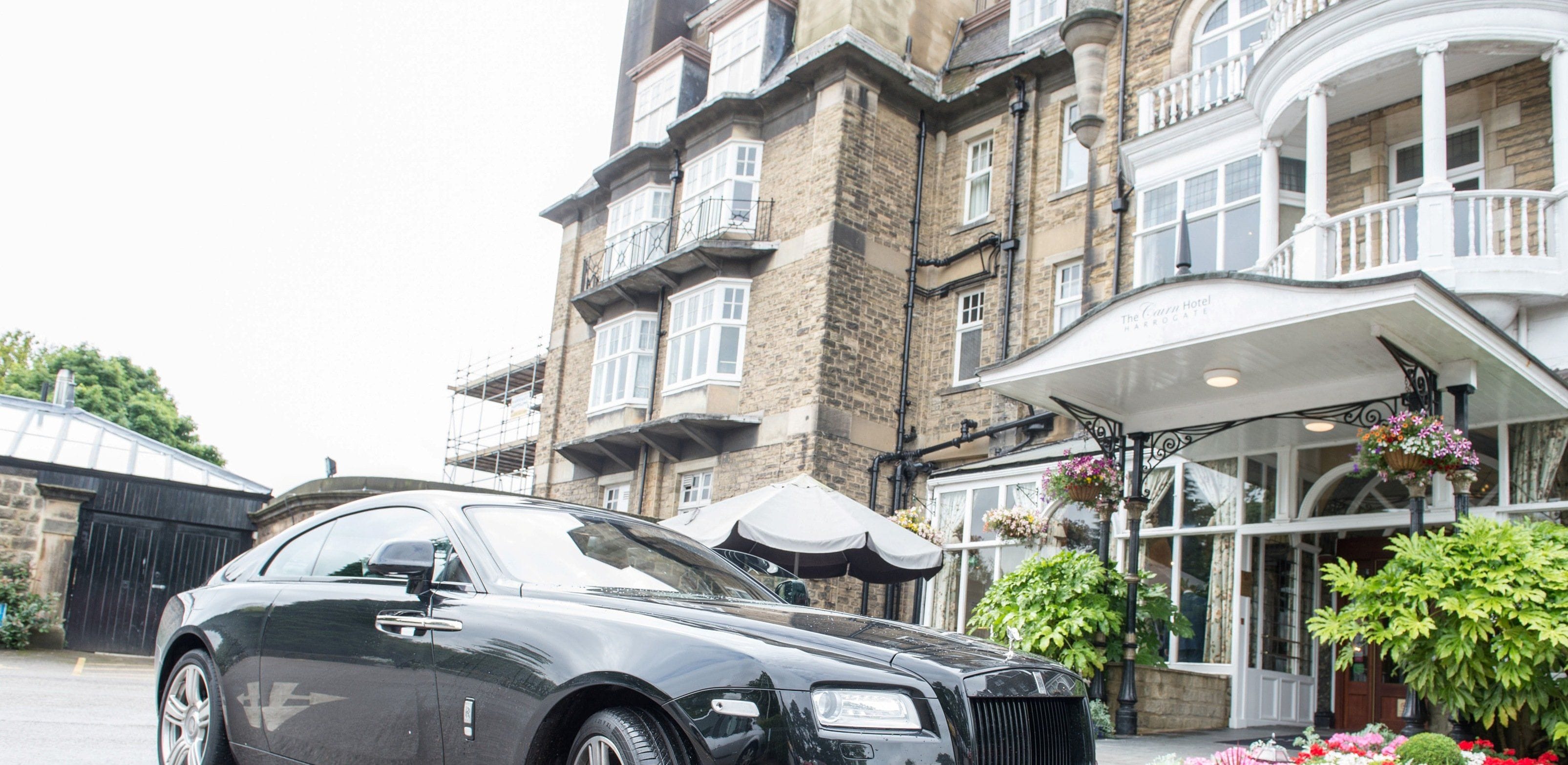 A luxury car parked in front of a historic building with a white facade and multiple windows.