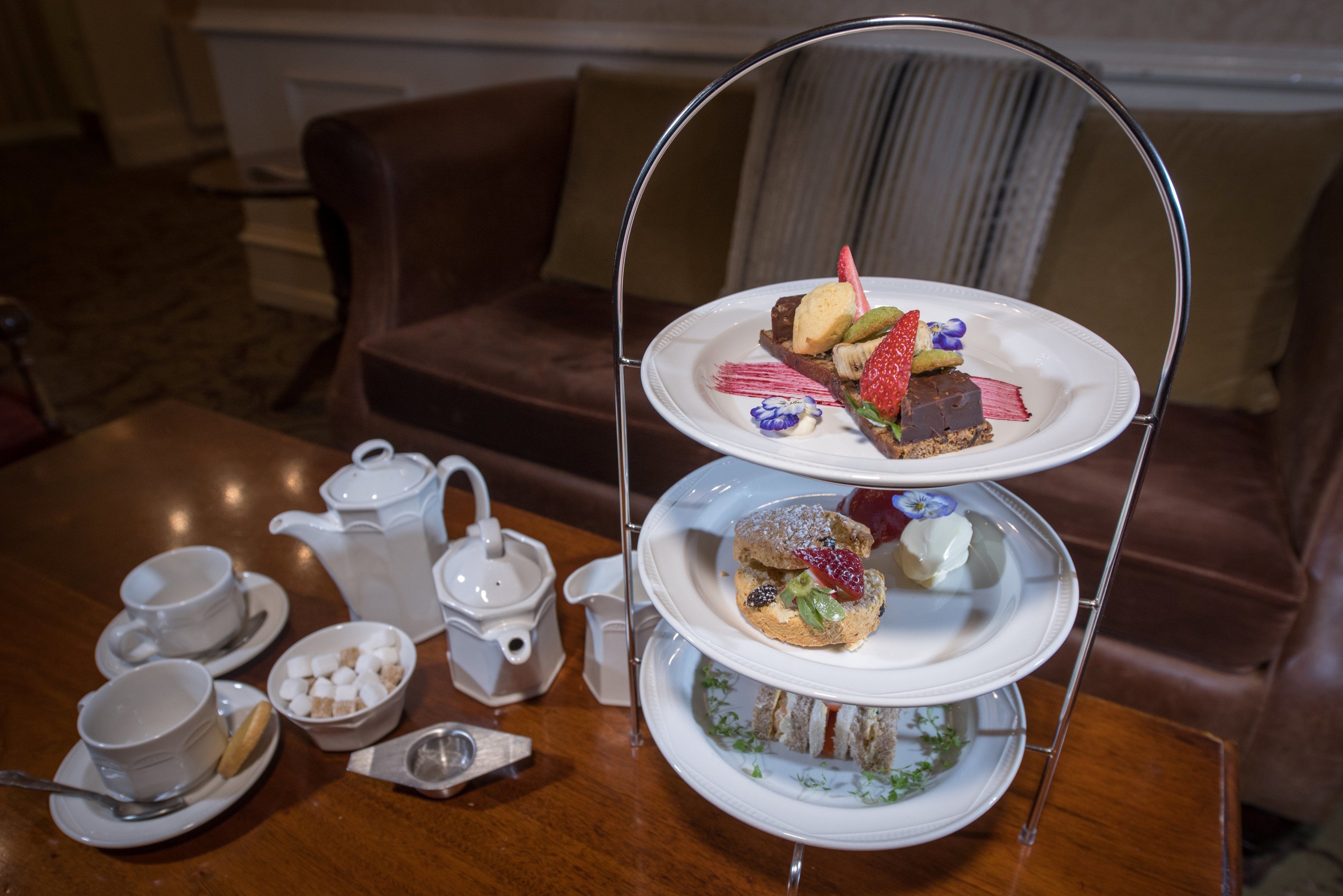 A three-tiered dessert stand with various pastries and a teapot on a table.