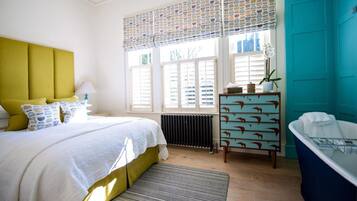Une chambre à coucher comprenant un lit, une table de chevet, une commode, un radiateur, une fenêtre avec des stores et une baignoire.