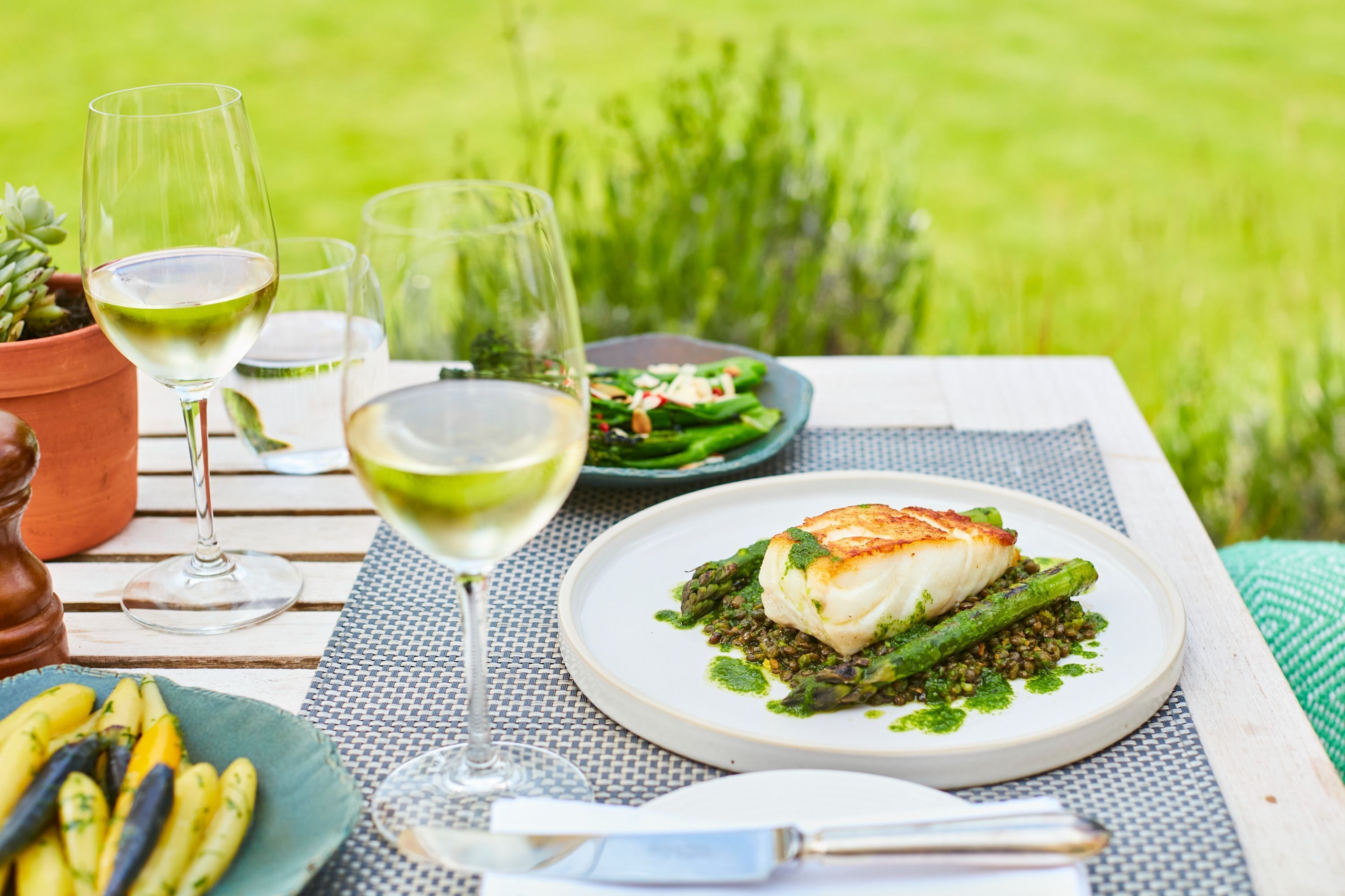 A dining table with a plate of food, wine glasses, and a potted plant.