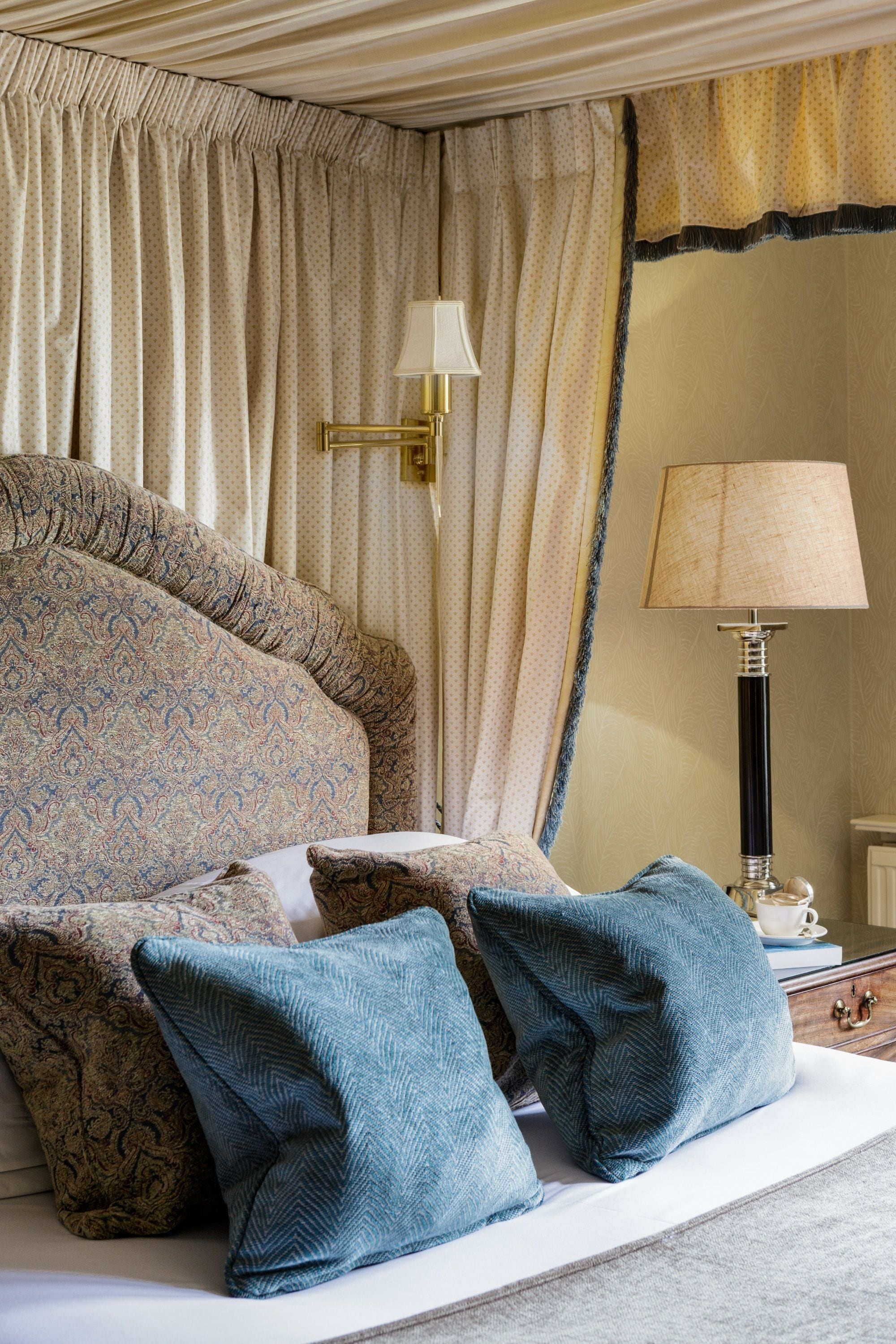 A bedroom with a large bed, patterned pillows, a bedside lamp, and curtains.