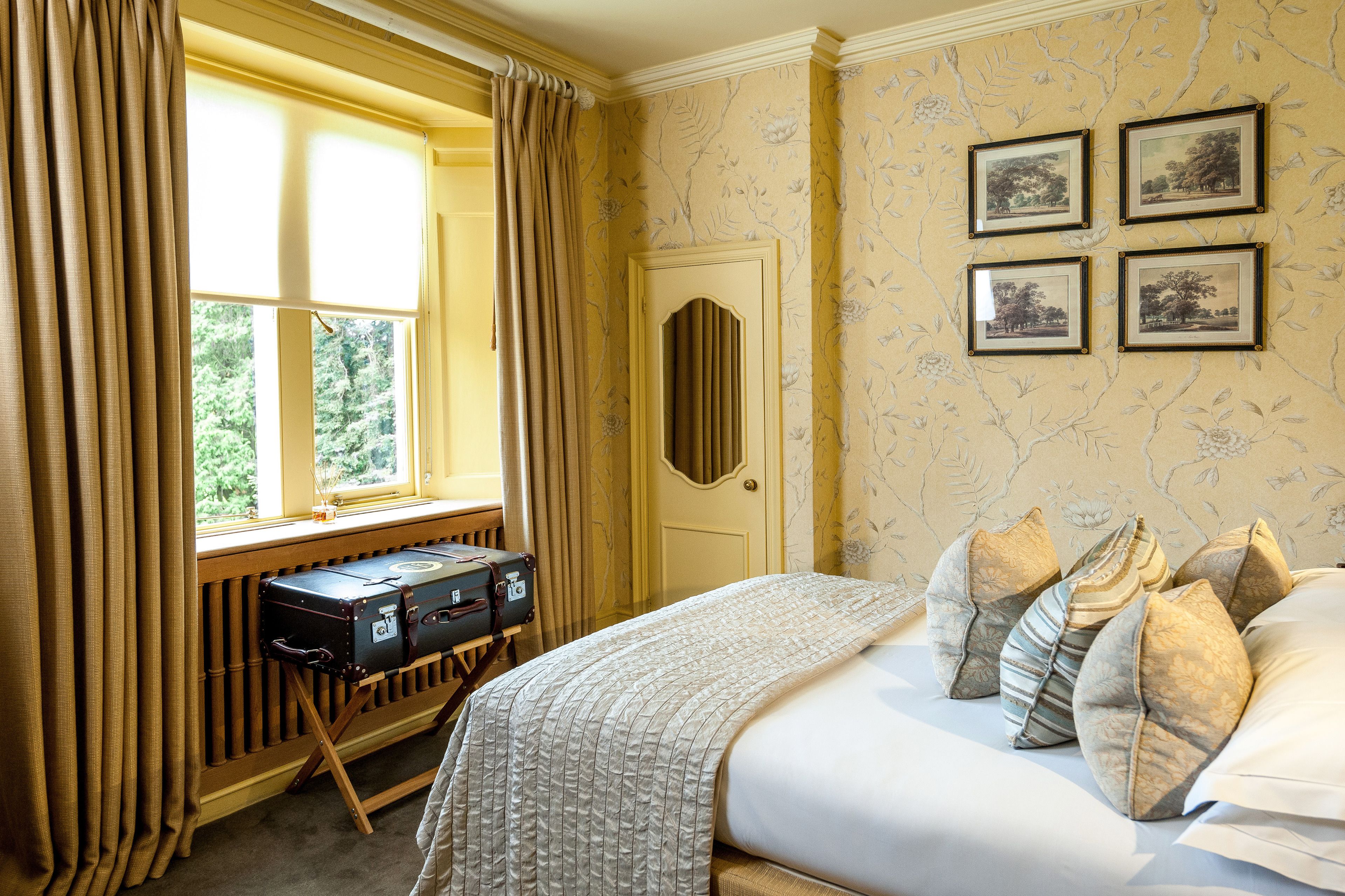 Een hotelkamer met een bed, een raam met gordijnen, een radiator en vier ingelijste foto's aan de muur.