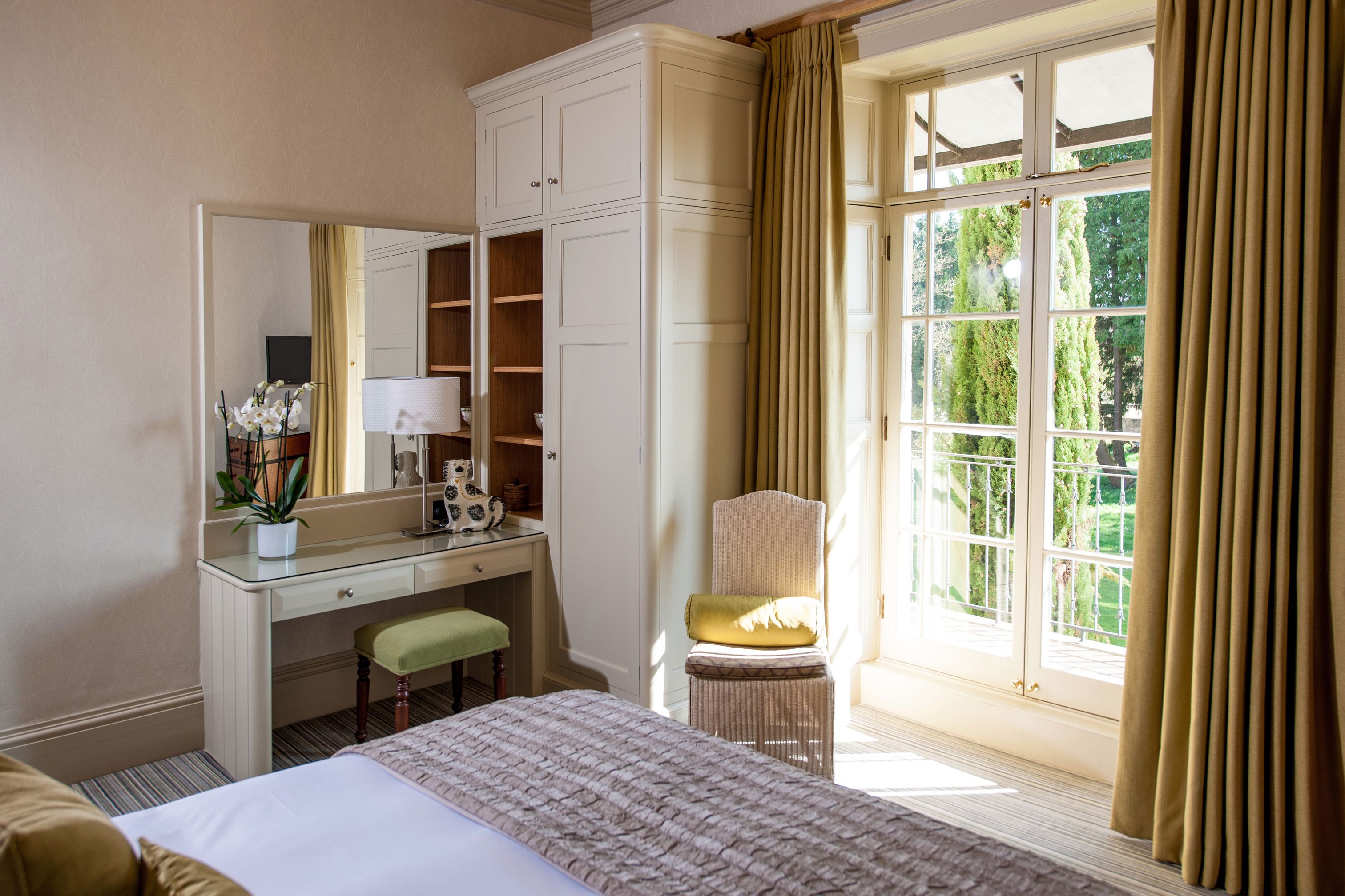 Une chambre d’hôtel comprenant un lit, un bureau avec une chaise, une armoire et une grande fenêtre avec des rideaux.