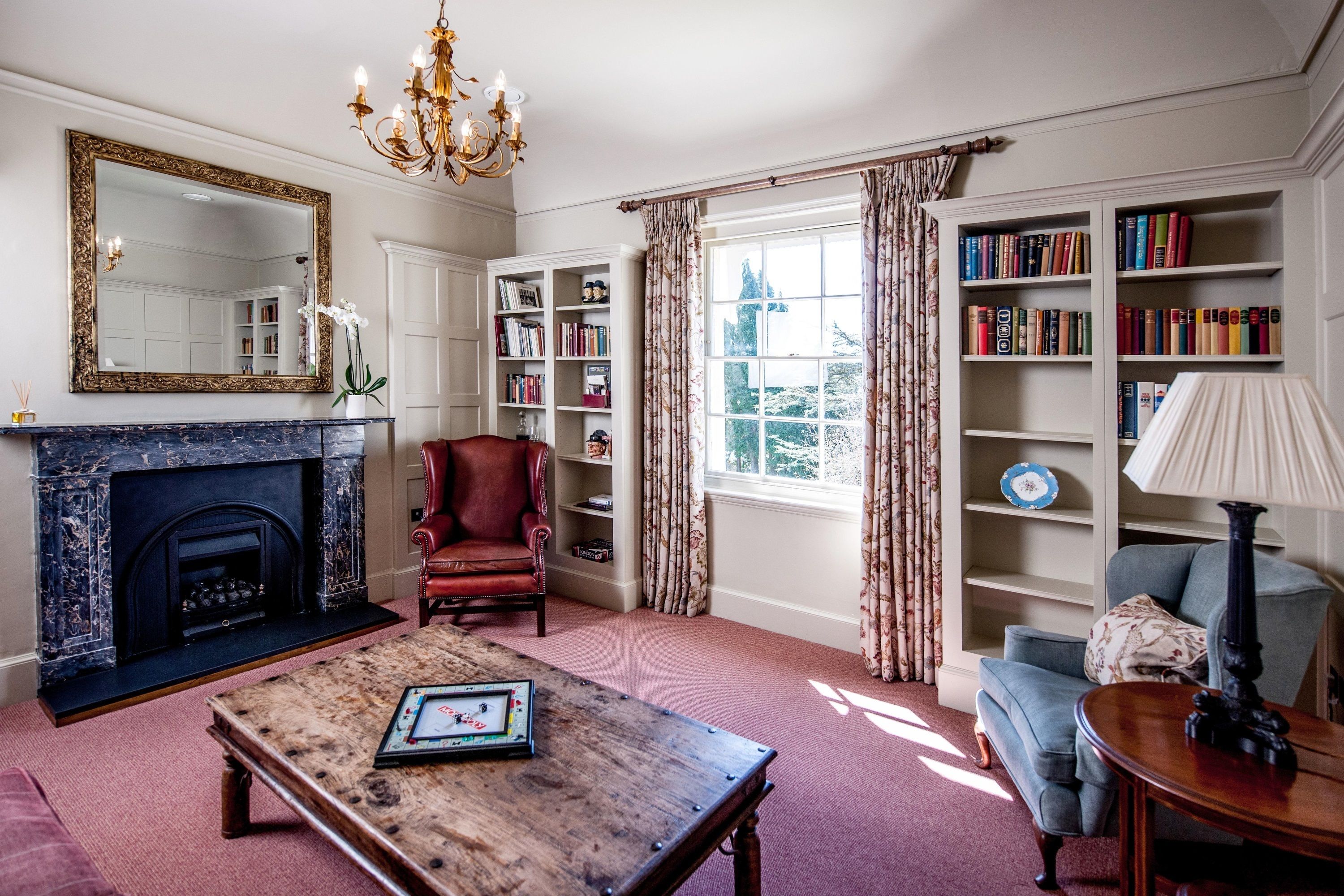 A living room with a fireplace, bookshelves, a red armchair, a blue armchair, and a wooden coffee table.