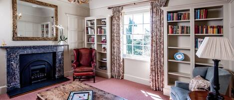 A living room with a fireplace, bookshelves, a red armchair, a blue armchair, and a wooden coffee table.